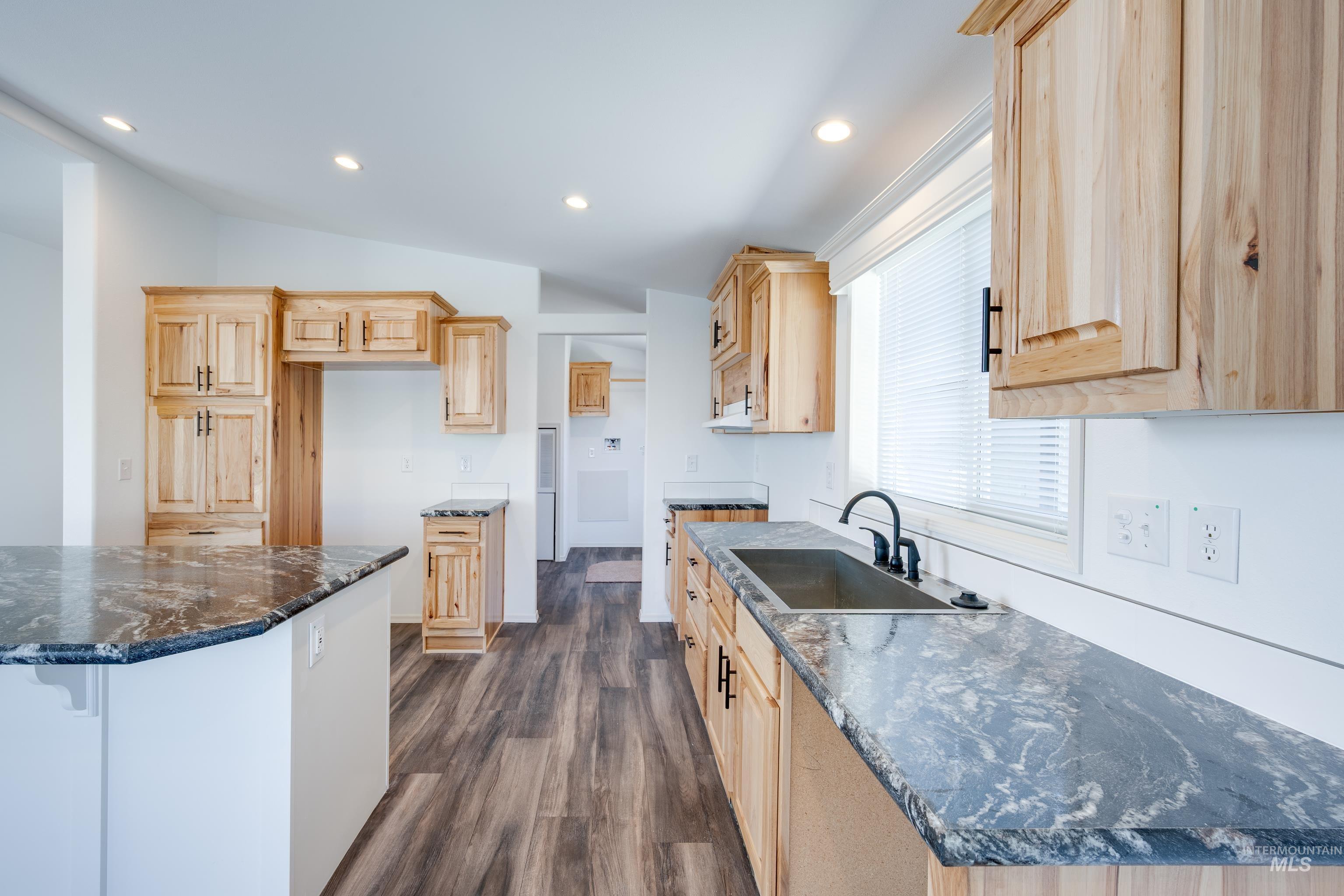 Kitchen with dark stone counters, light brown cabinets, recessed lighting, dark wood-style floors, and vaulted ceiling
