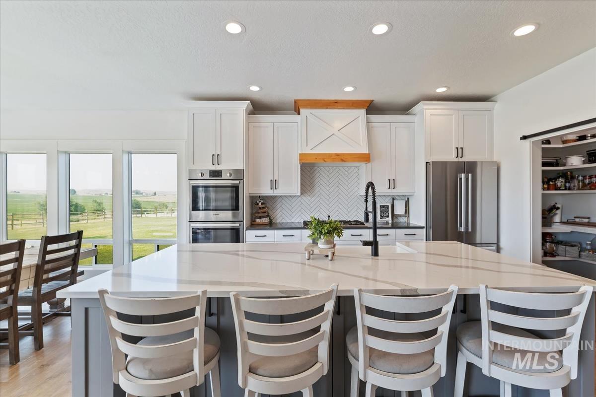Kitchen featuring appliances with stainless steel finishes, white cabinetry, recessed lighting, decorative backsplash, and a spacious island
