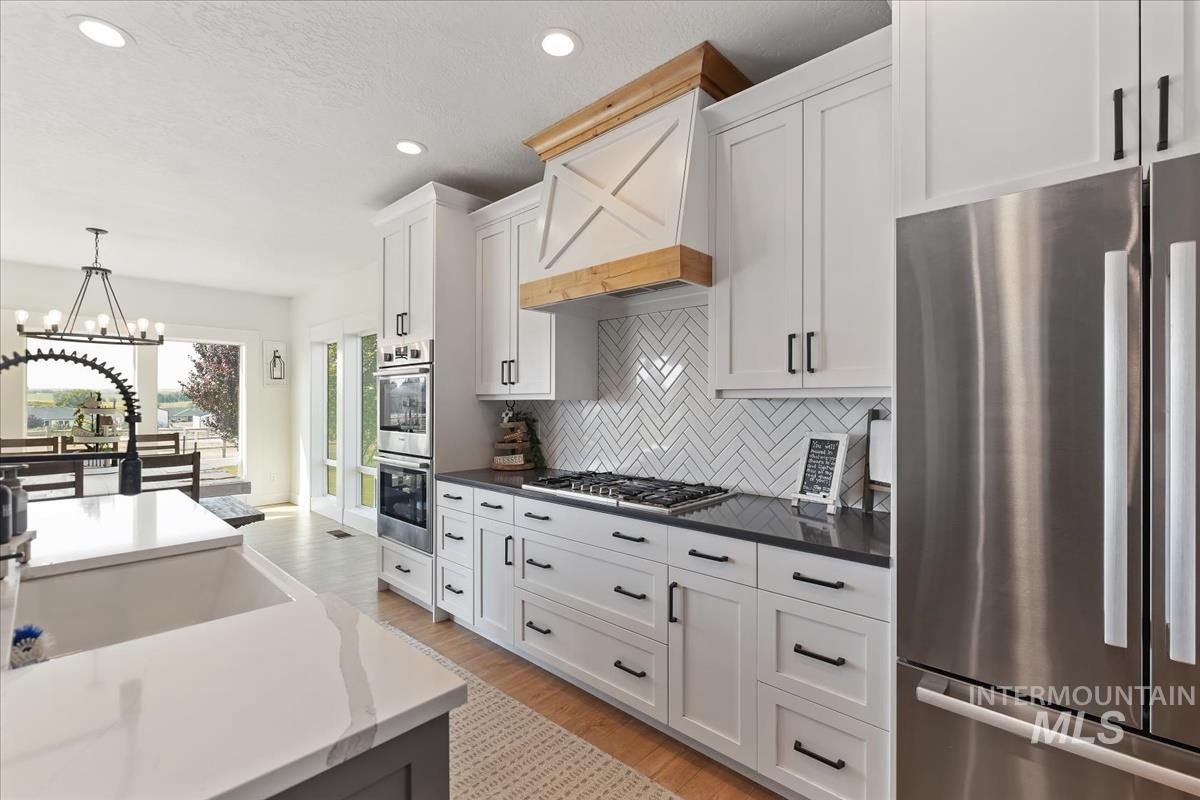Kitchen with stainless steel appliances, light wood-style floors, pendant lighting, a chandelier, and white cabinetry