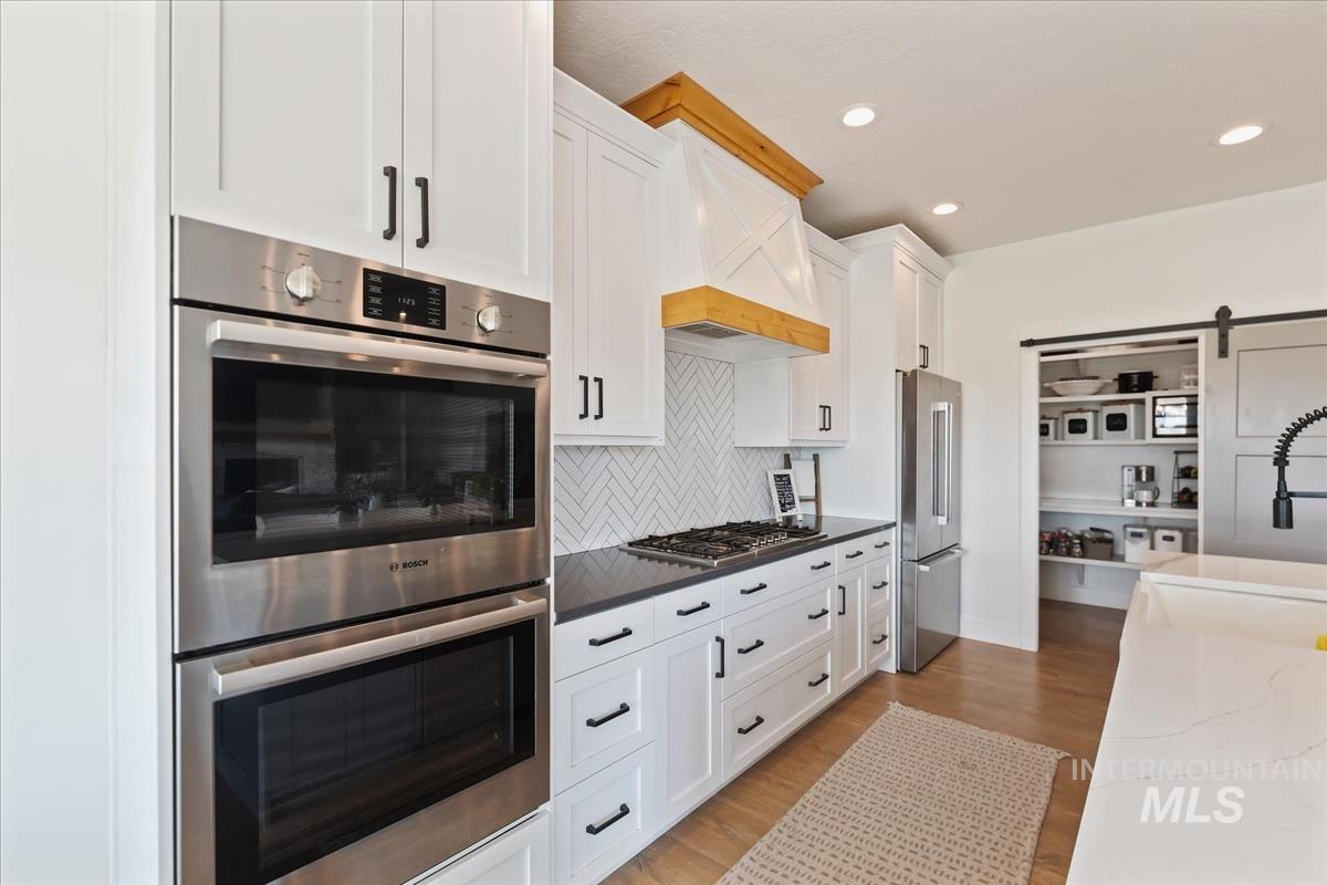 Kitchen with stainless steel appliances, a barn door, white cabinets, light wood-style floors, and dark stone counters