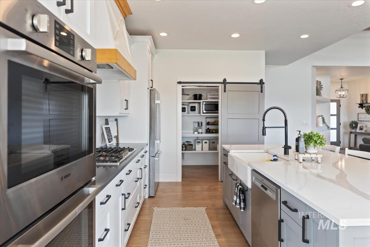 Kitchen with white cabinets, stainless steel appliances, recessed lighting, light wood finished floors, and a barn door