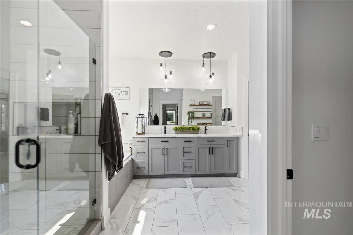 Bathroom featuring a stall shower, double vanity, light marble finish flooring, and recessed lighting