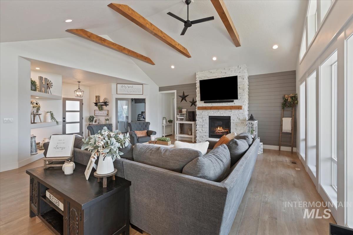 Living room with a stone fireplace, beamed ceiling, recessed lighting, high vaulted ceiling, and ceiling fan