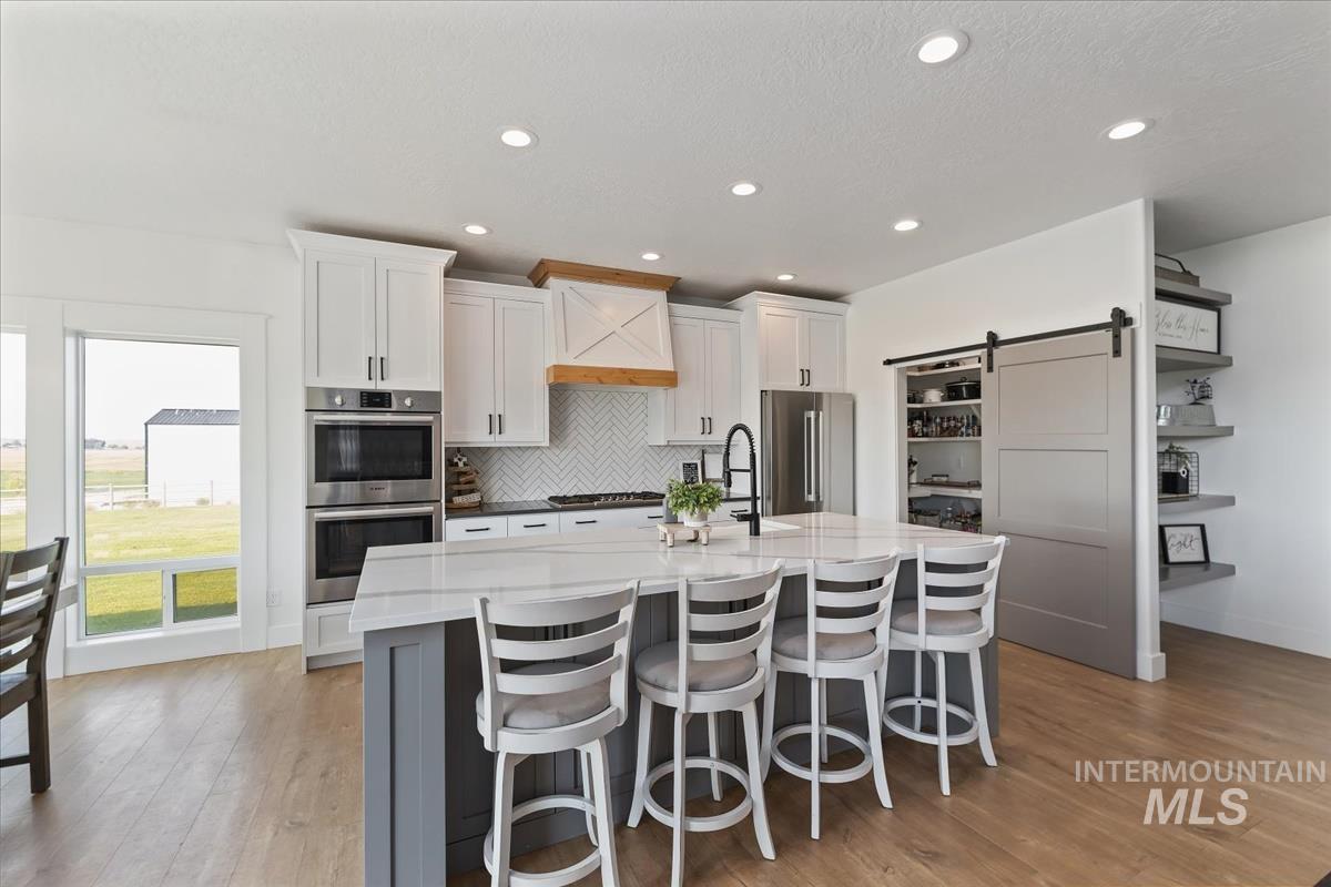 Kitchen featuring a barn door, white cabinetry, a breakfast bar, a large island with sink, and stainless steel appliances