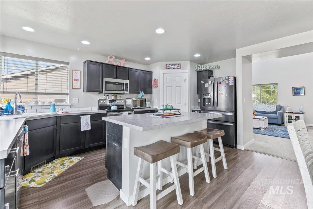 Kitchen featuring light countertops, appliances with stainless steel finishes, dark wood finished floors, a kitchen bar, and recessed lighting