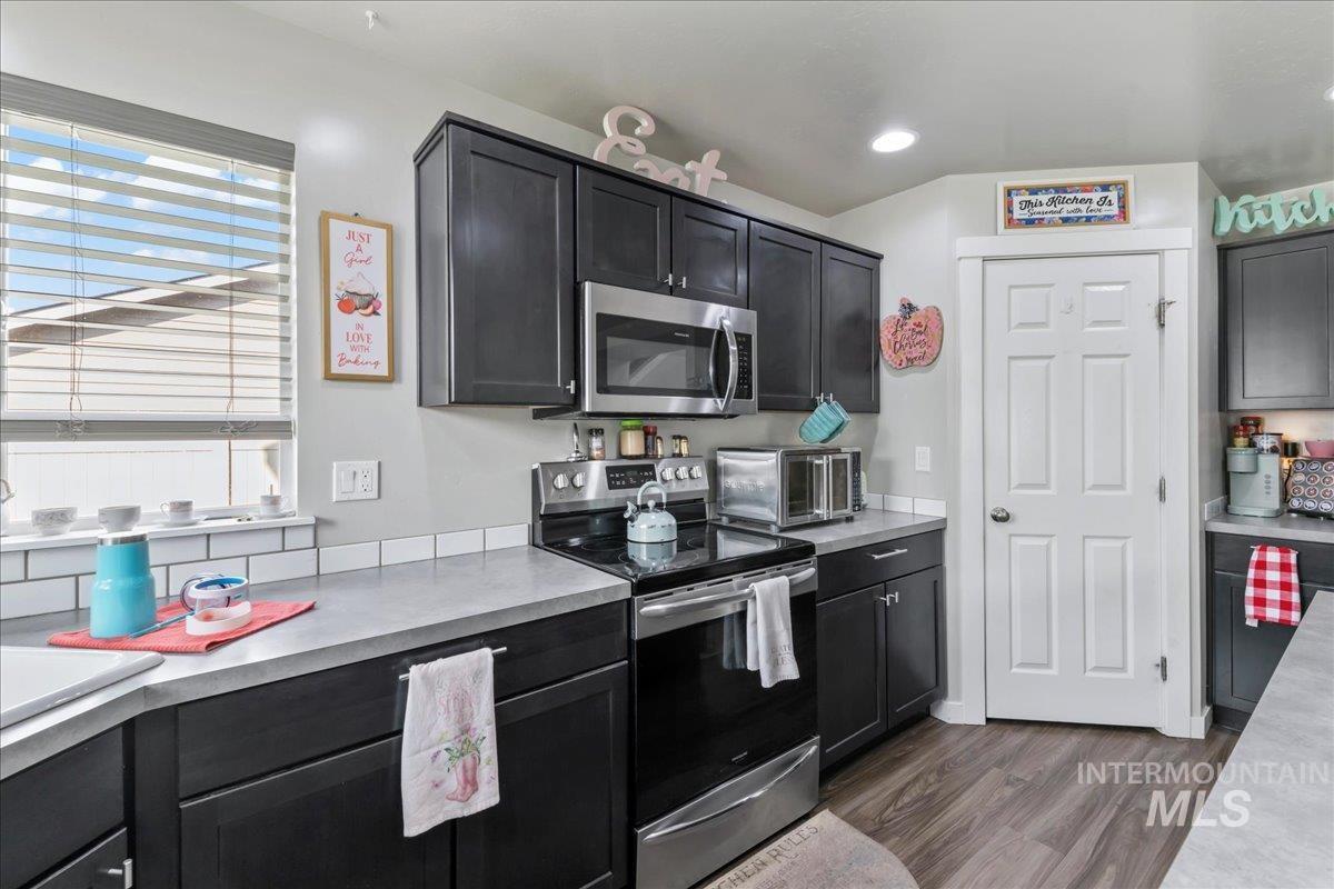 Kitchen featuring appliances with stainless steel finishes, light countertops, dark wood-style floors, and dark cabinets