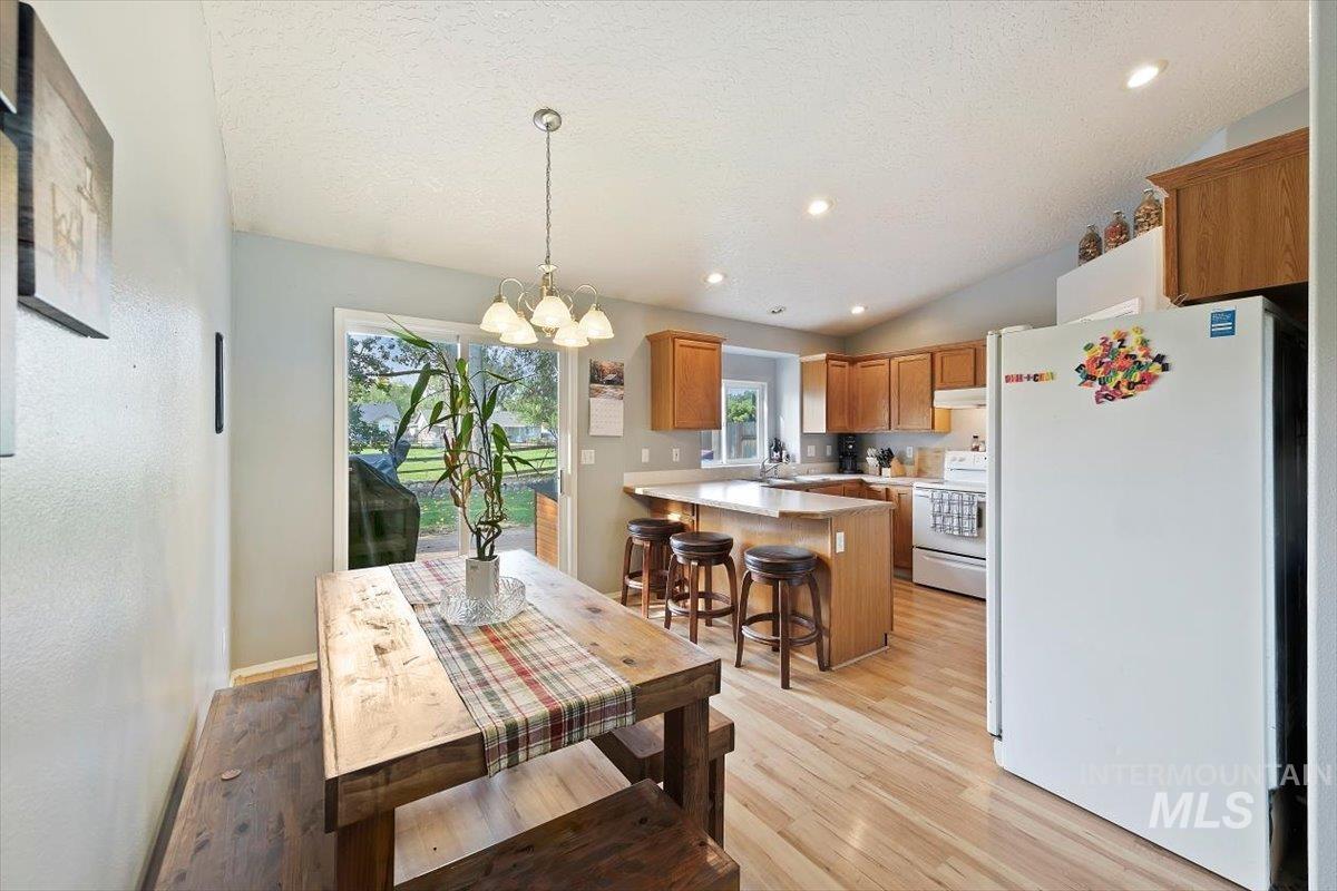 Dining space with light wood-type flooring, a chandelier, lofted ceiling, recessed lighting, and a textured ceiling