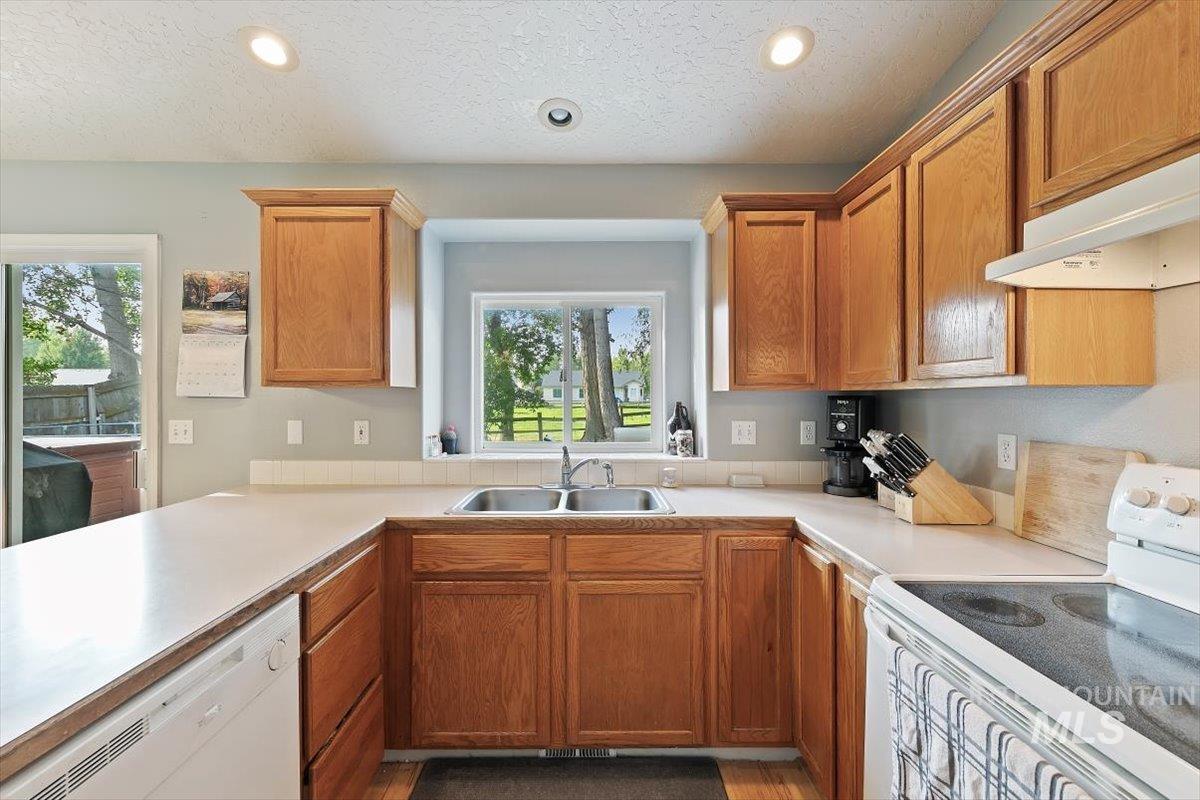 Kitchen featuring white appliances, light countertops, brown cabinetry, recessed lighting, and a textured ceiling