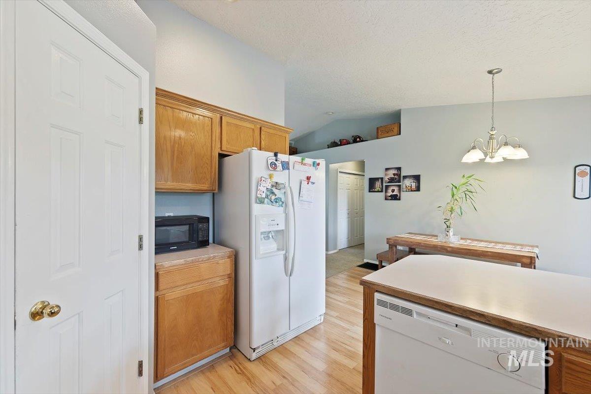 Kitchen with white appliances, light countertops, brown cabinets, hanging light fixtures, and light wood finished floors