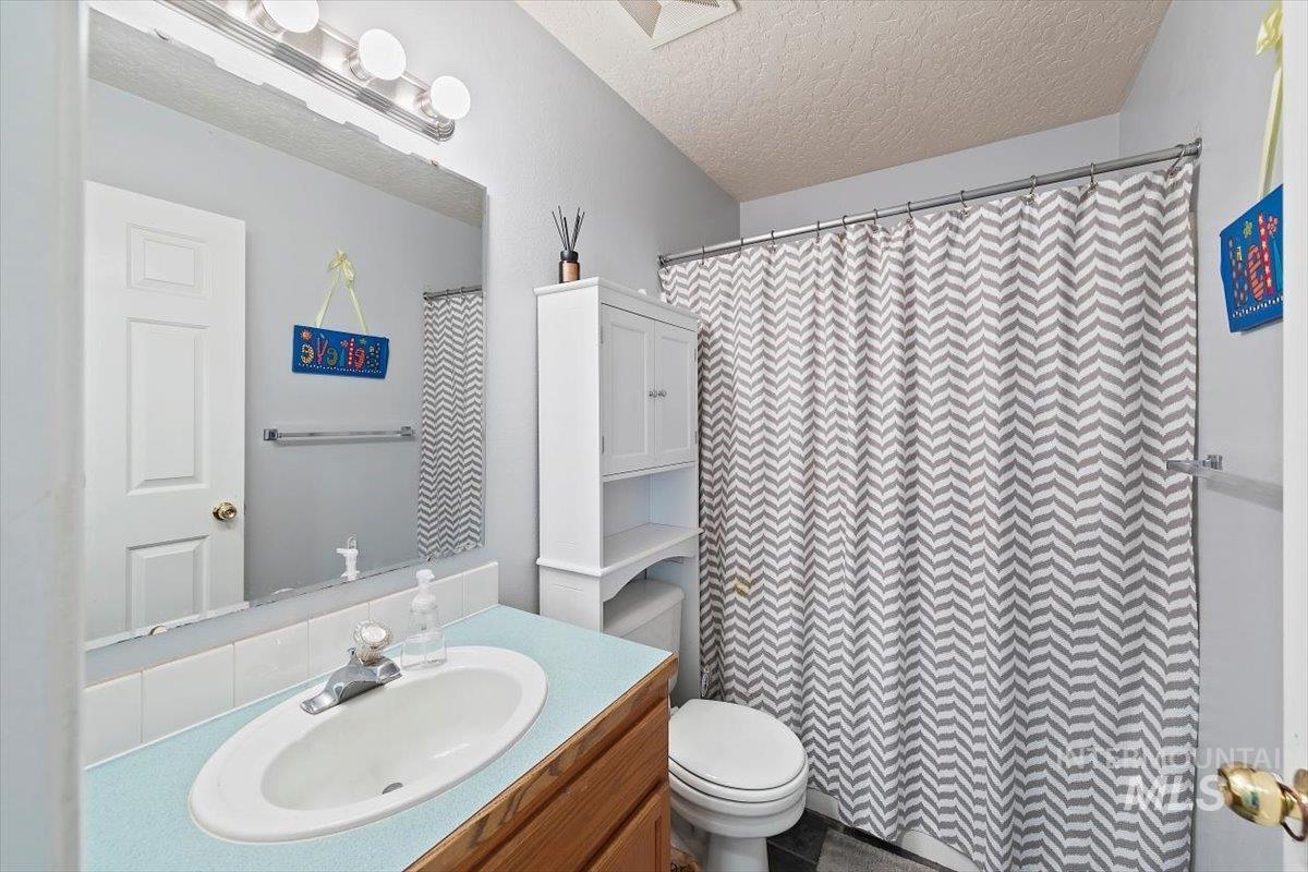 Bathroom featuring a textured ceiling, vanity, and curtained shower