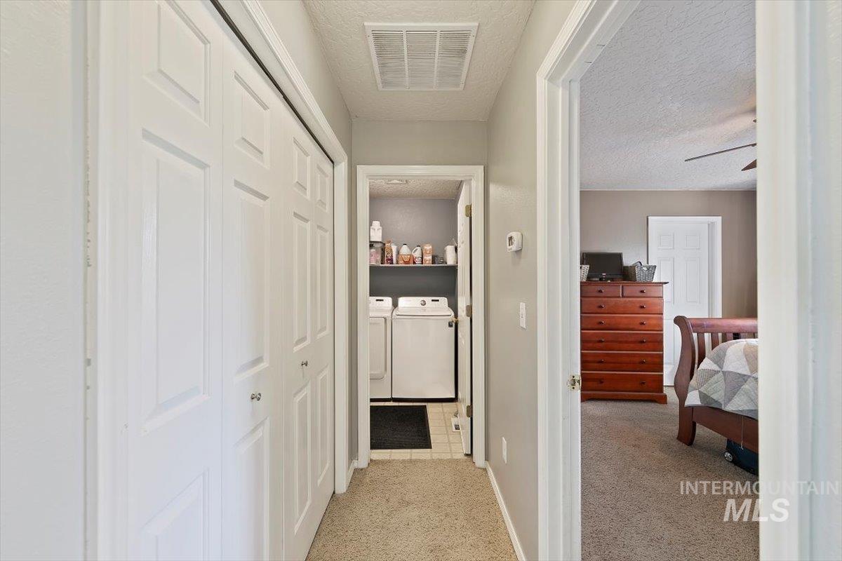 Hallway featuring light carpet, a textured ceiling, and washing machine and dryer
