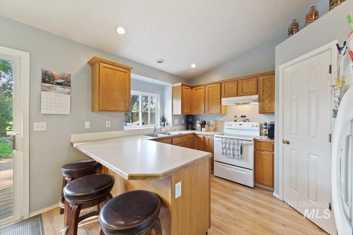 Kitchen with light countertops, white appliances, a peninsula, a kitchen bar, and lofted ceiling