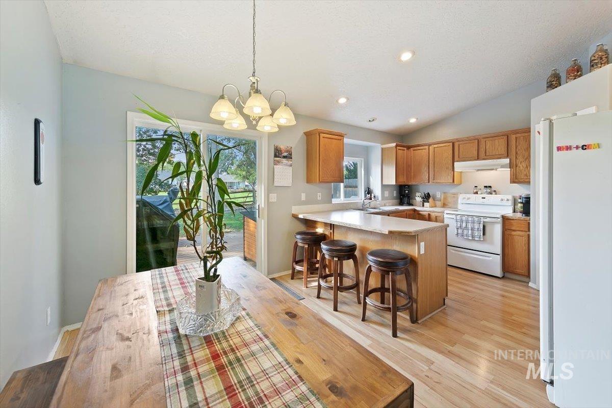 Kitchen featuring white appliances, hanging light fixtures, light countertops, a kitchen breakfast bar, and vaulted ceiling