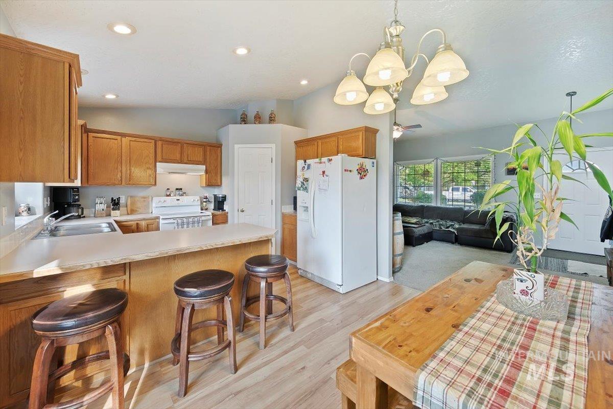 Kitchen with a breakfast bar, a peninsula, white appliances, pendant lighting, and light countertops