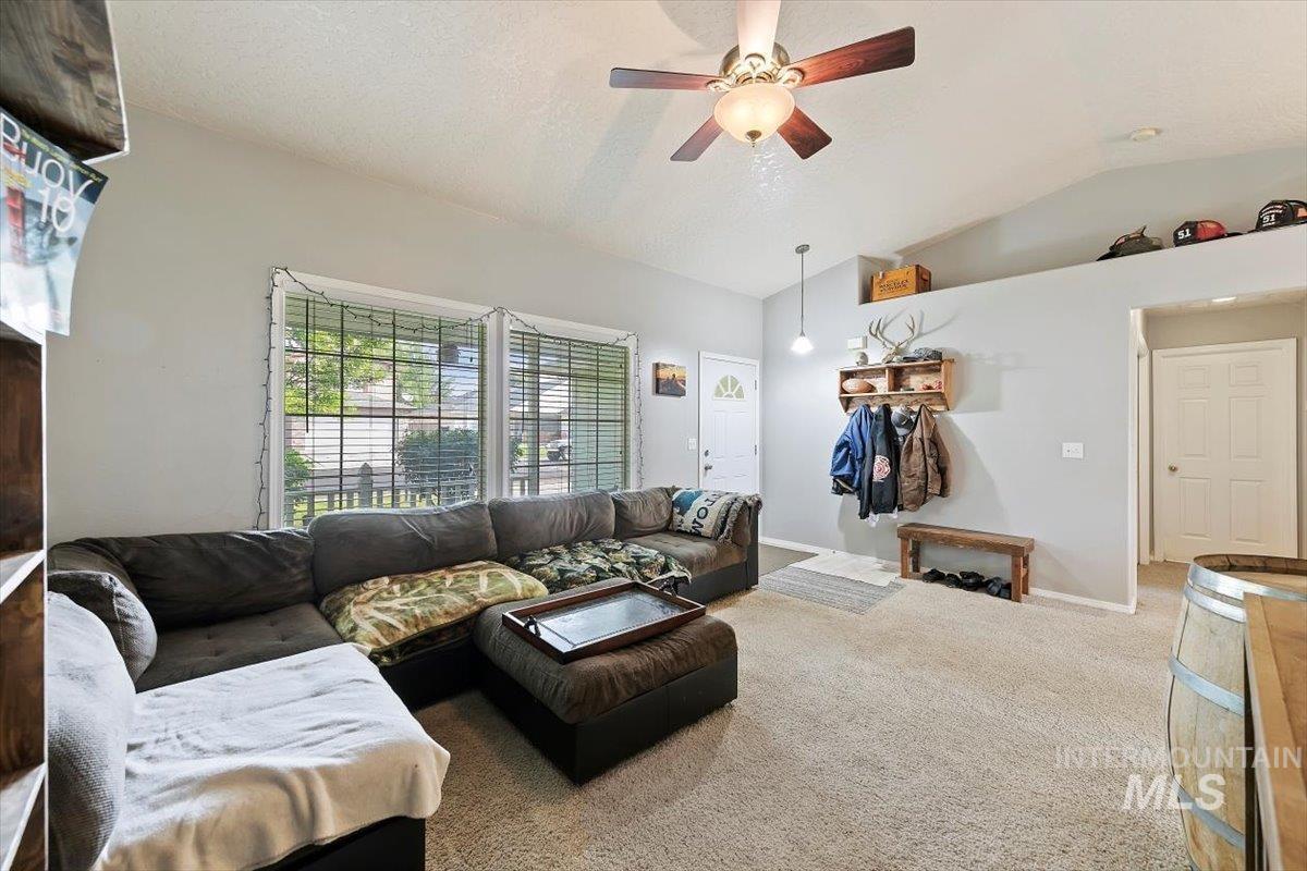 Carpeted living room featuring vaulted ceiling, ceiling fan, and a textured ceiling