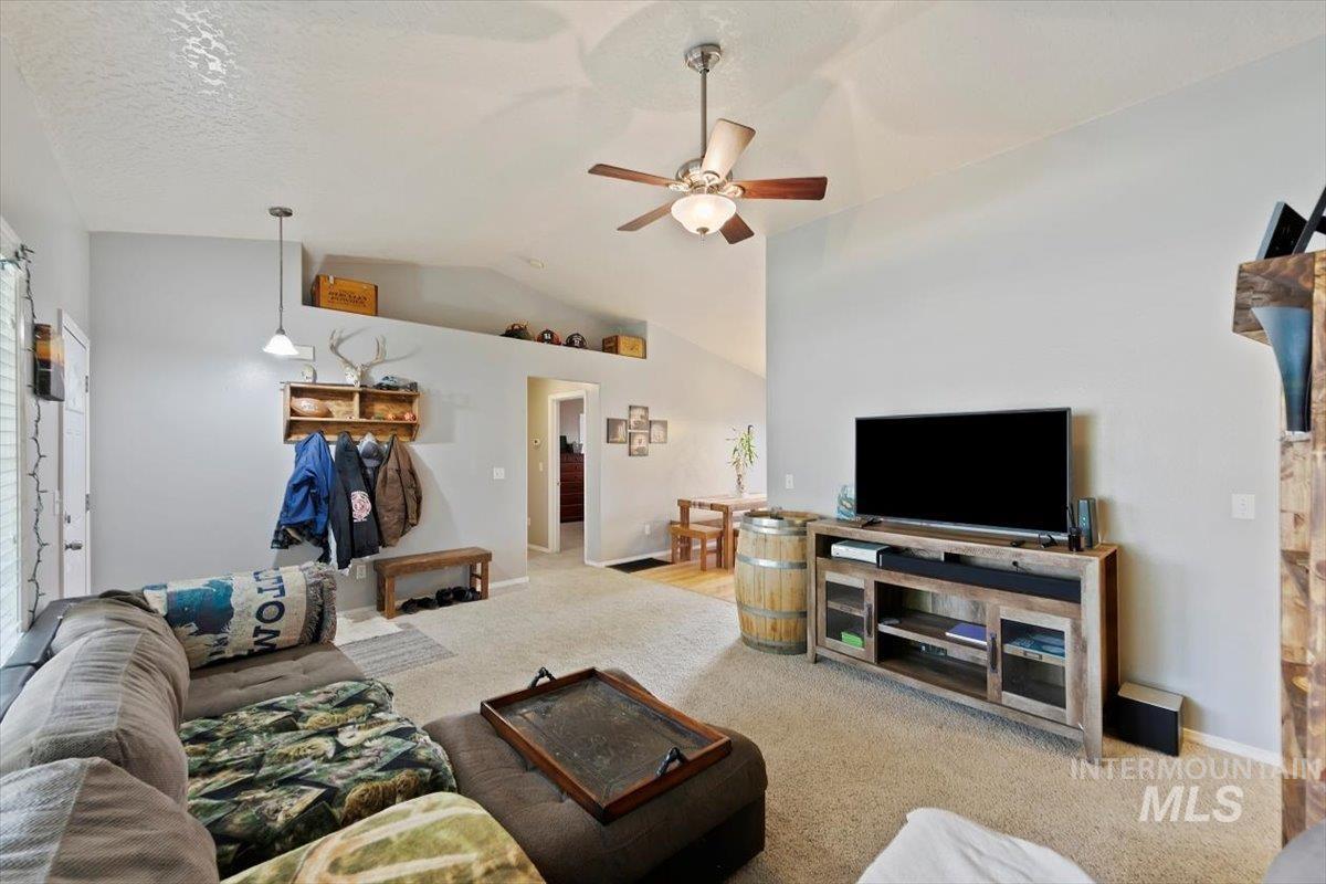 Living room featuring light colored carpet, a ceiling fan, a textured ceiling, and high vaulted ceiling
