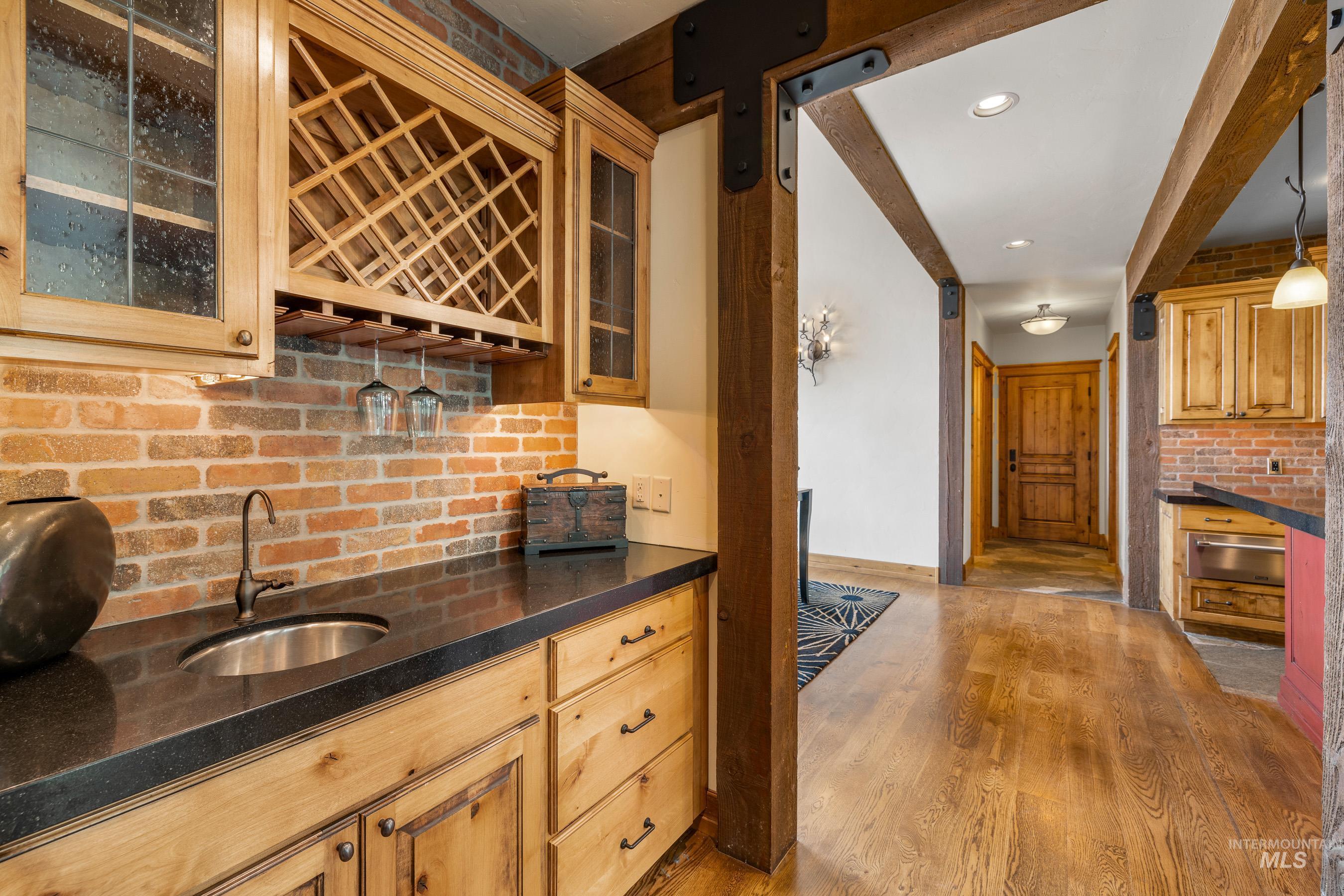 Indoor wet bar featuring light wood-type flooring, tasteful backsplash, decorative light fixtures, glass insert cabinets, and recessed lighting
