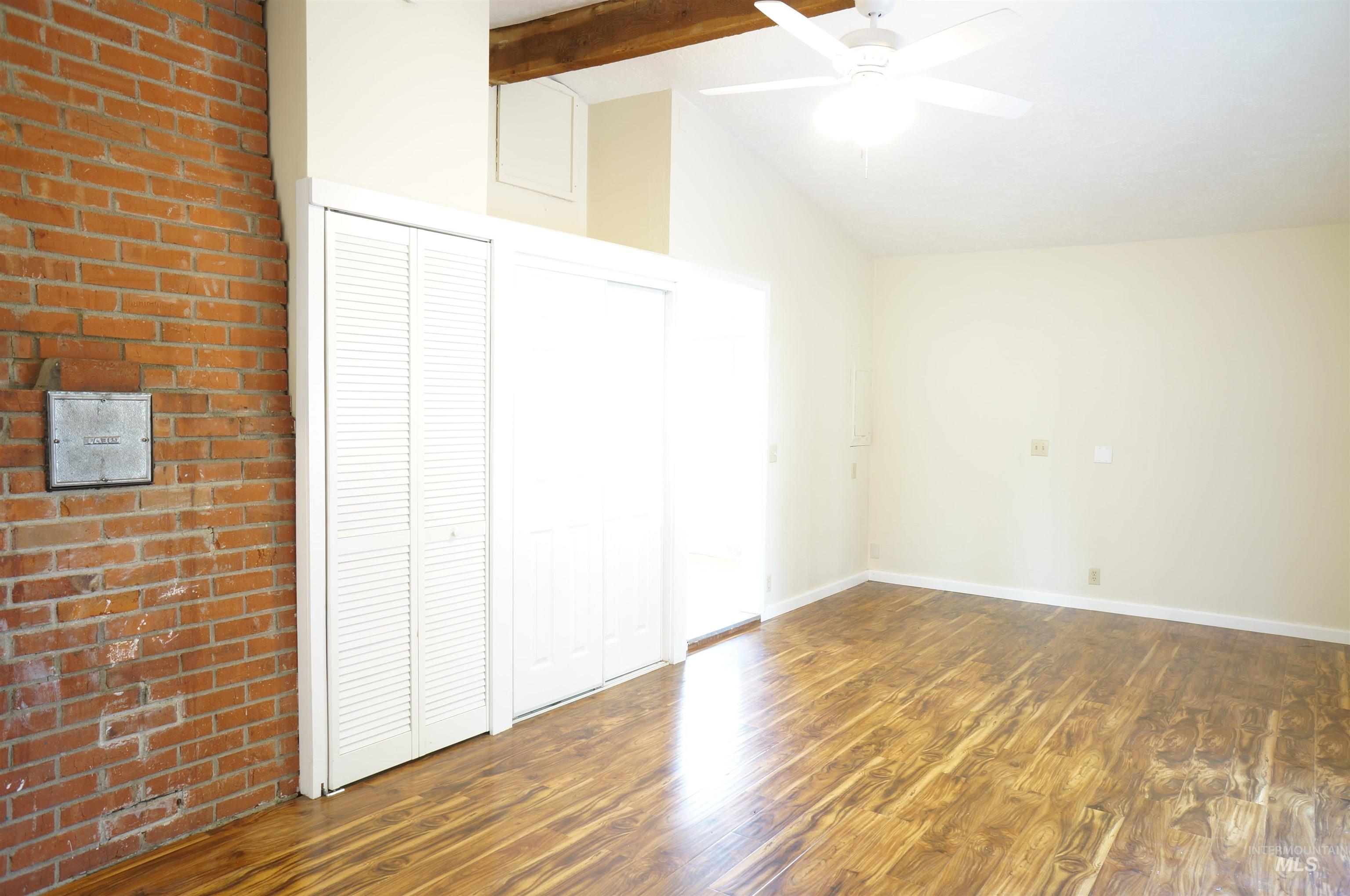 Unfurnished bedroom with dark wood-style flooring, ceiling fan, and brick wall