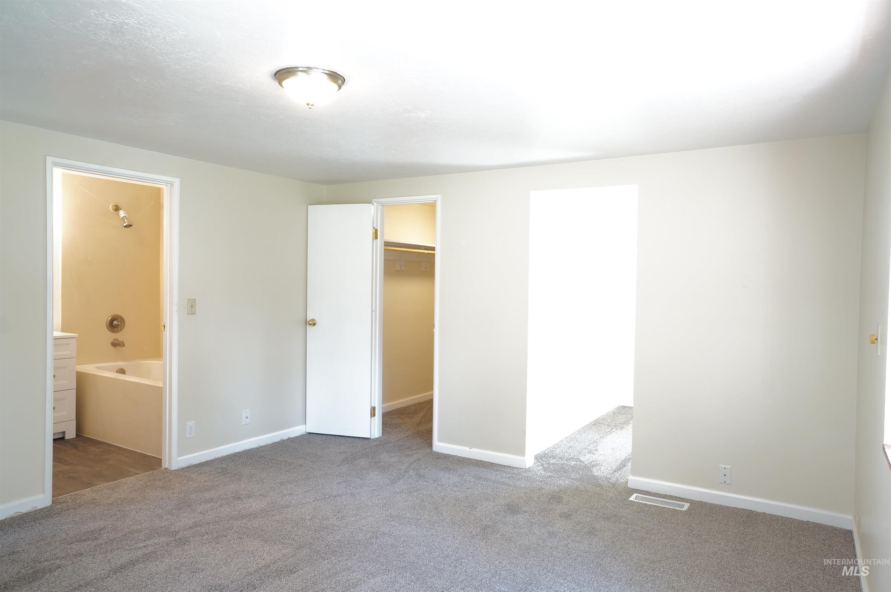 Unfurnished bedroom featuring a walk in closet, carpet floors, and ensuite bathroom