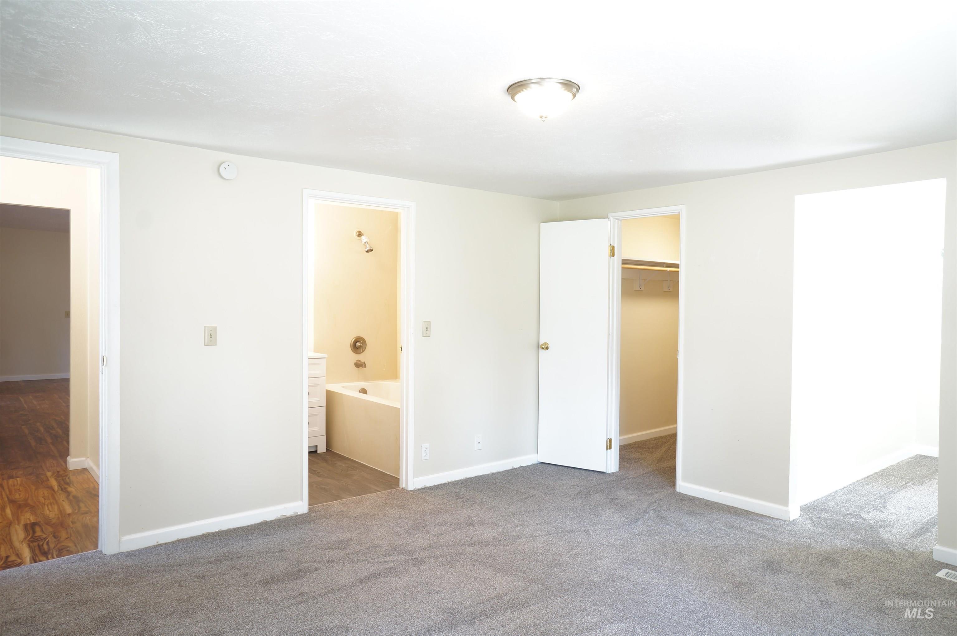 Unfurnished bedroom with a walk in closet, ensuite bathroom, and carpet flooring