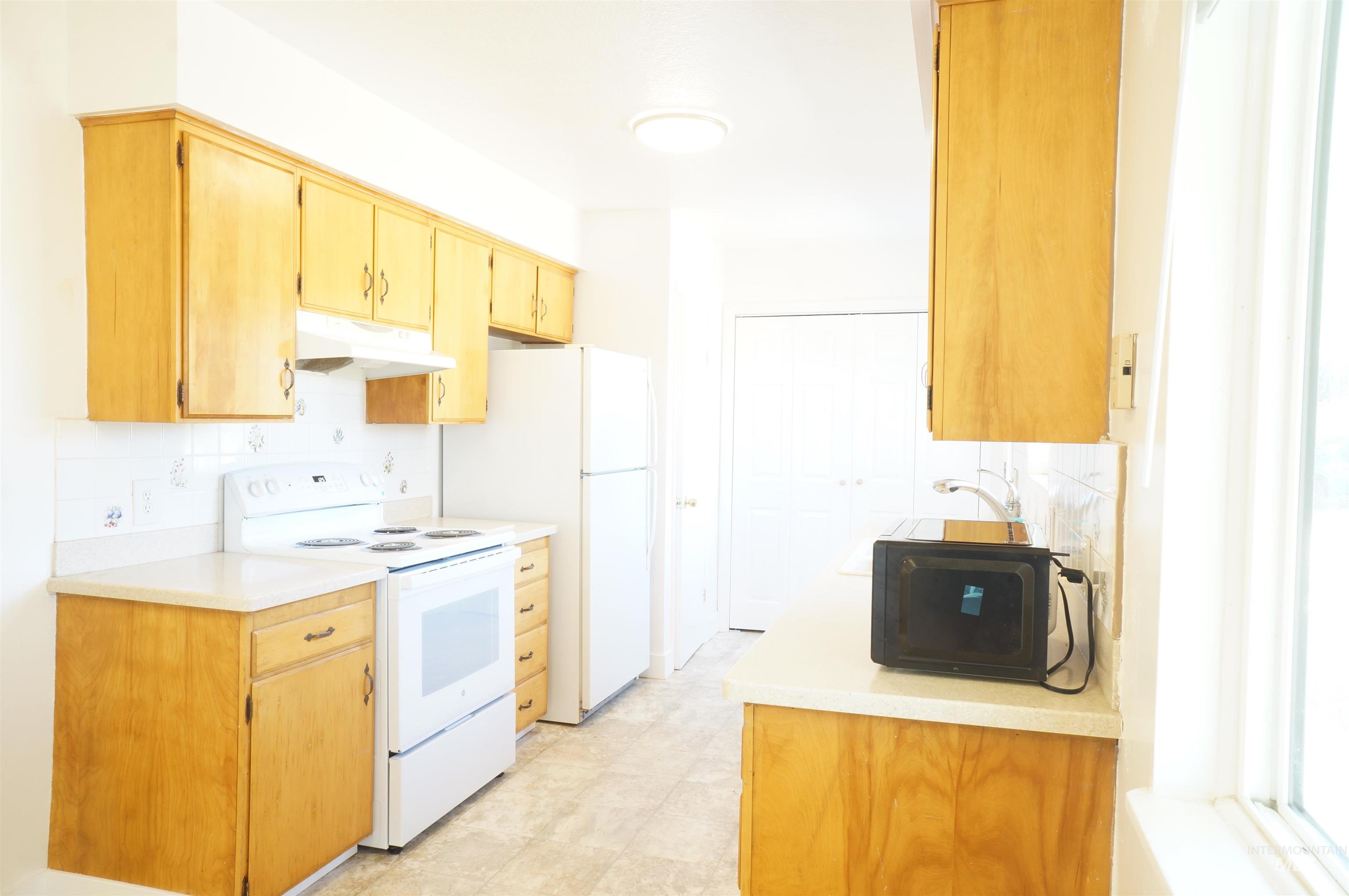 Kitchen with white appliances, under cabinet range hood, and decorative backsplash