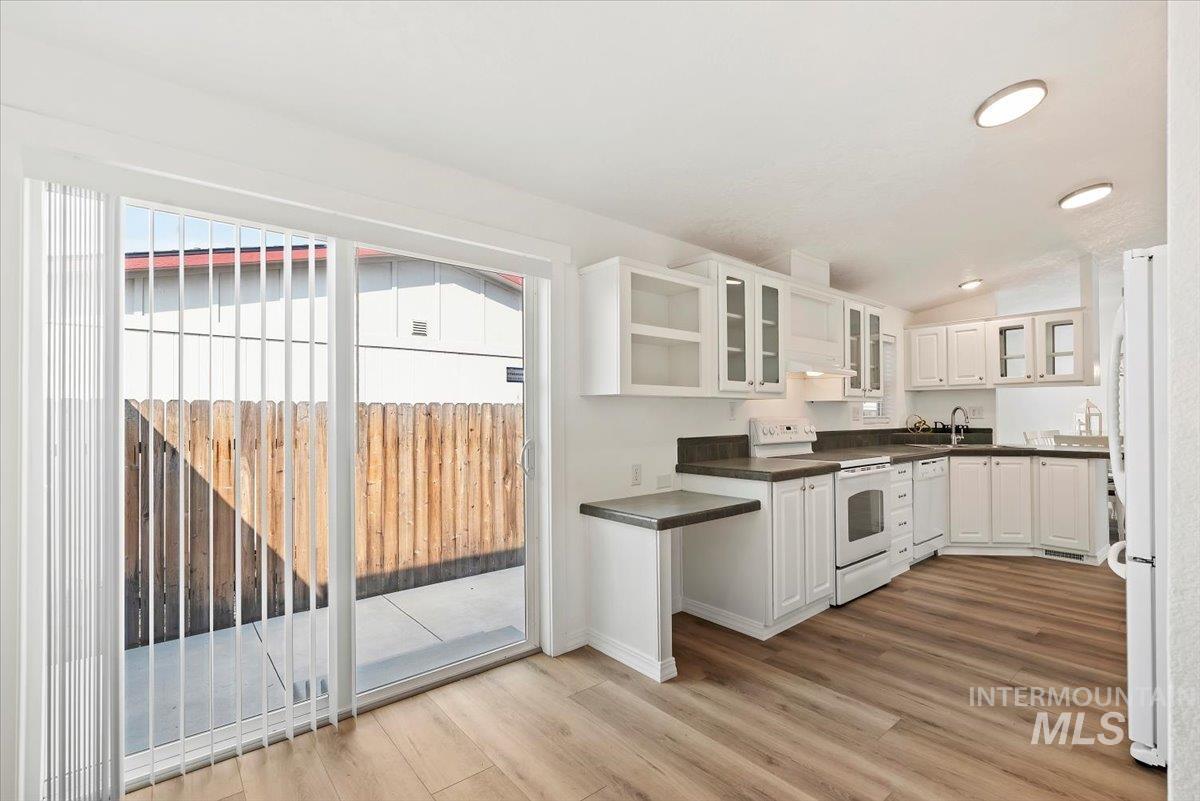 Kitchen featuring white cabinets, dark countertops, white appliances, light wood-style flooring, and vaulted ceiling