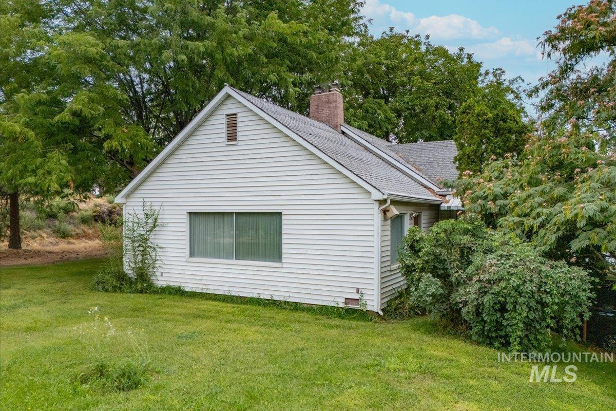 View of property exterior featuring a lawn, a chimney, a shingled roof, and view of wooded area
