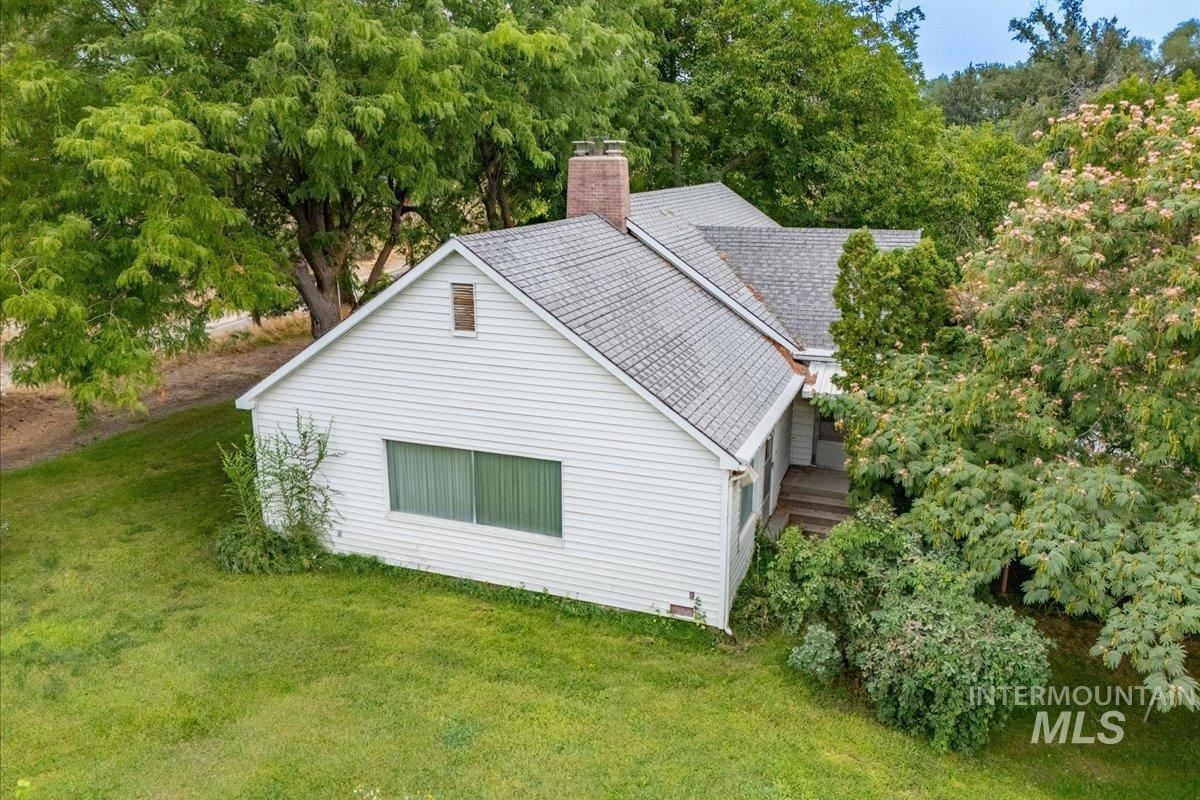 View of side of home featuring a chimney, a lawn, a shingled roof, and view of wooded area
