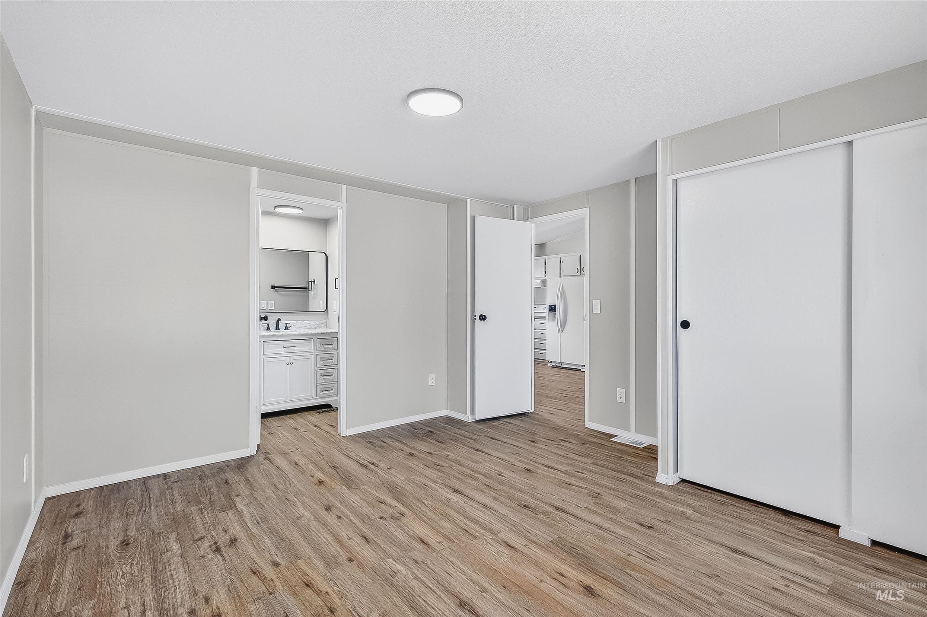 Unfurnished bedroom with light wood-style flooring, white refrigerator with ice dispenser, a closet, and ensuite bathroom