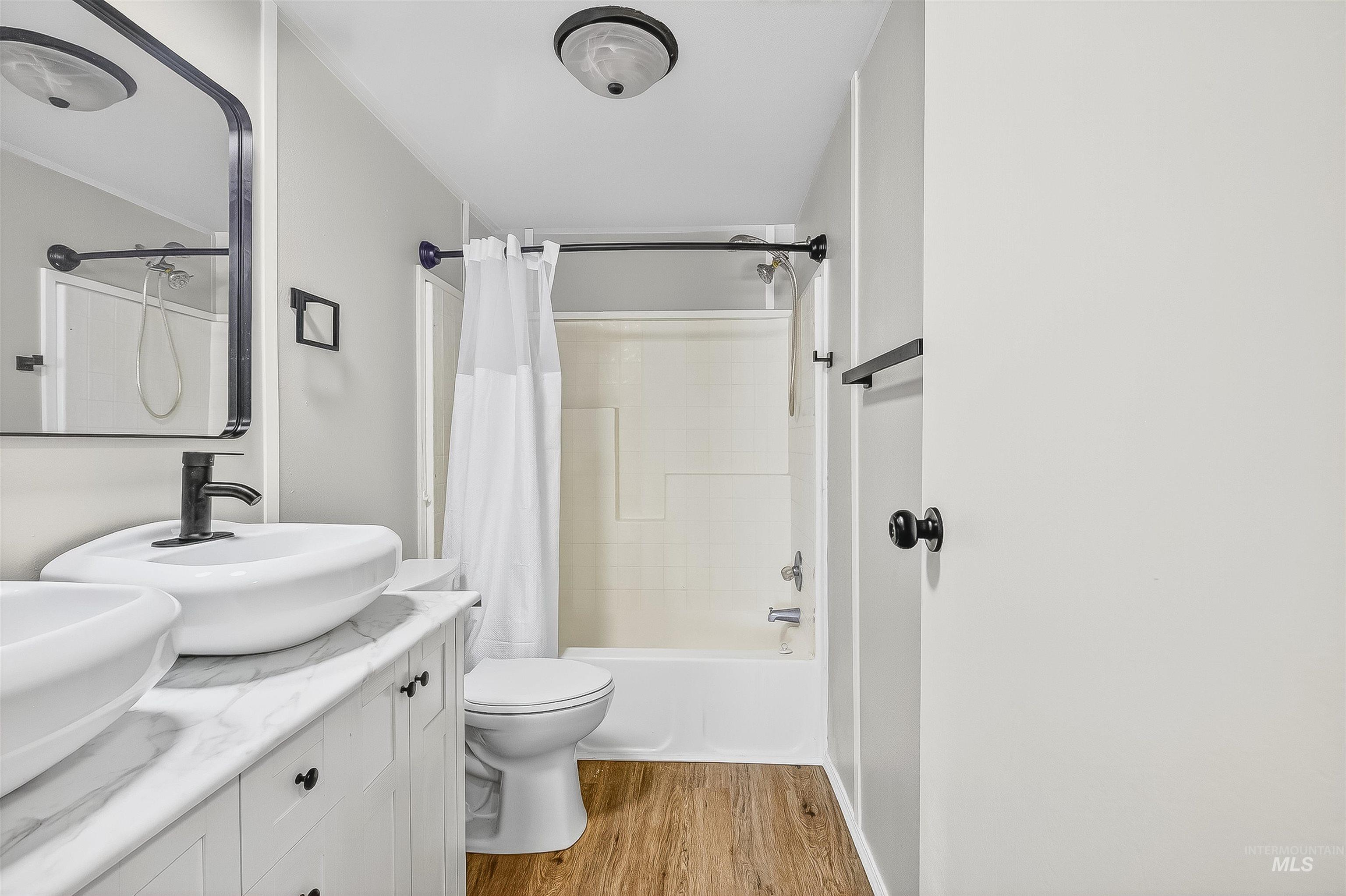 Full bath featuring shower / bath combination with curtain, light wood-type flooring, and double vanity
