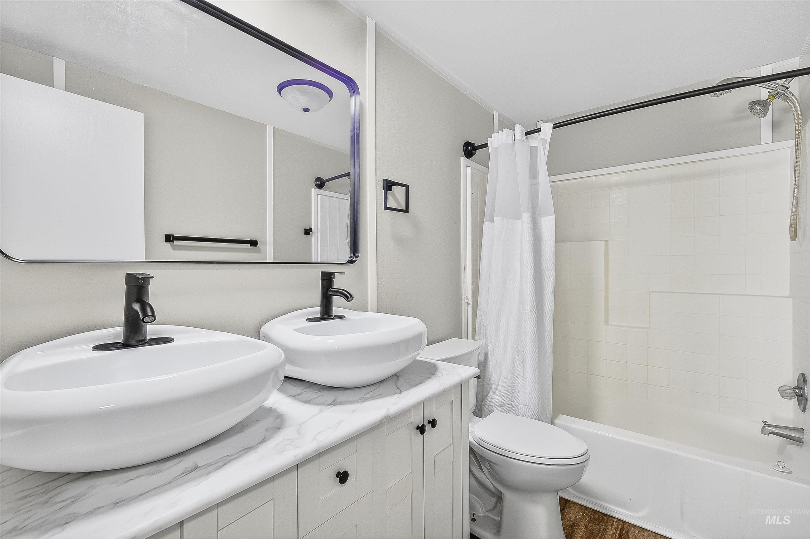 Bathroom featuring shower / bath combo with shower curtain, double vanity, and dark wood finished floors