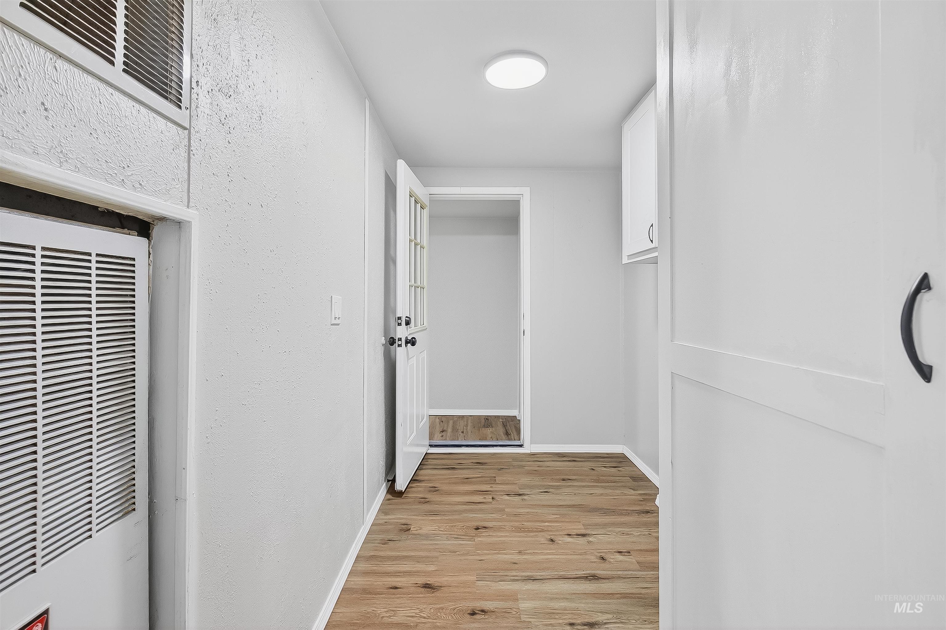 Hallway featuring a heating unit, light wood finished floors, and a textured wall
