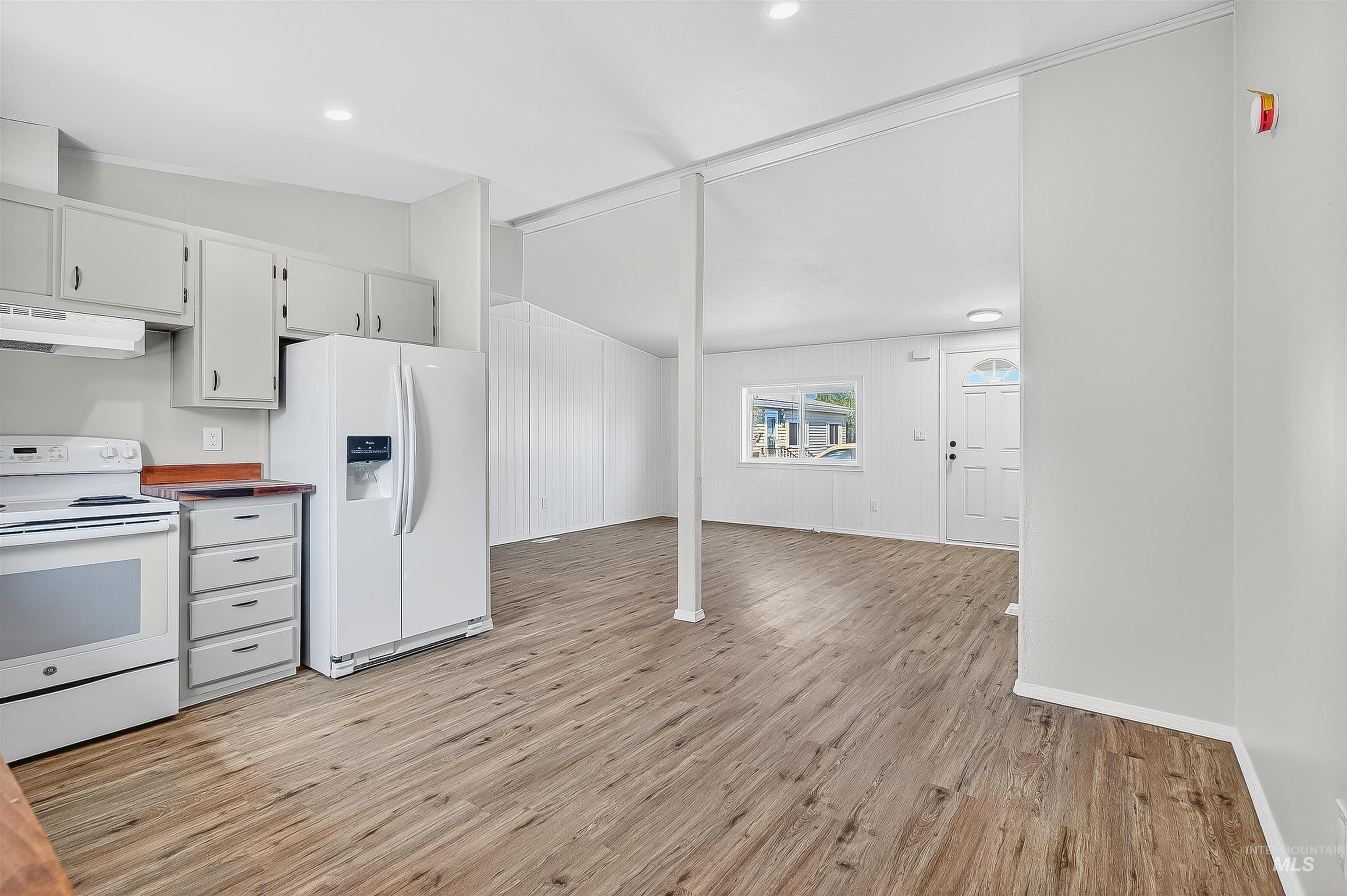 Kitchen with white appliances, light wood-type flooring, lofted ceiling, under cabinet range hood, and wooden counters