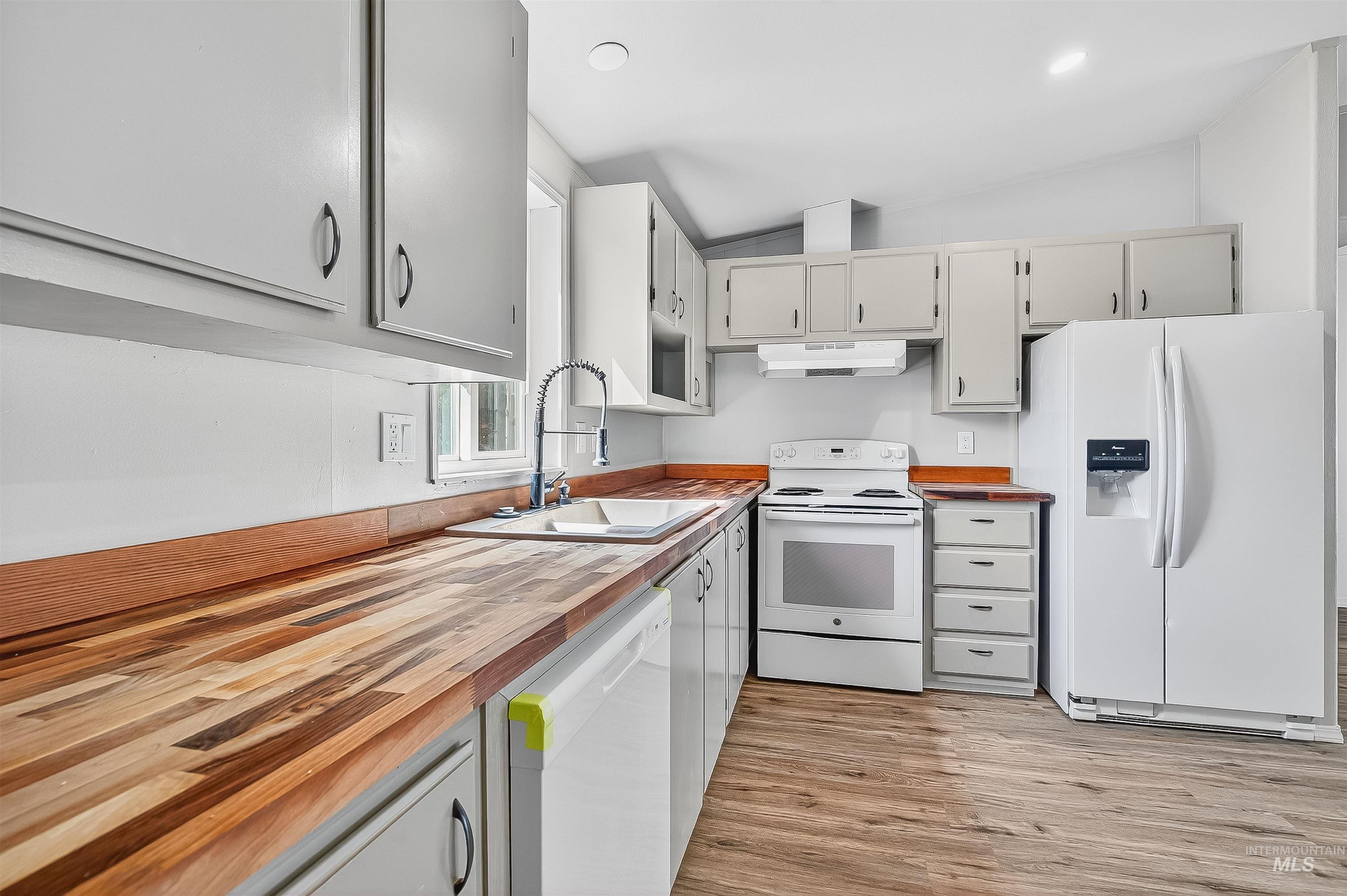 Kitchen with white appliances, butcher block countertops, vaulted ceiling, light wood finished floors, and under cabinet range hood