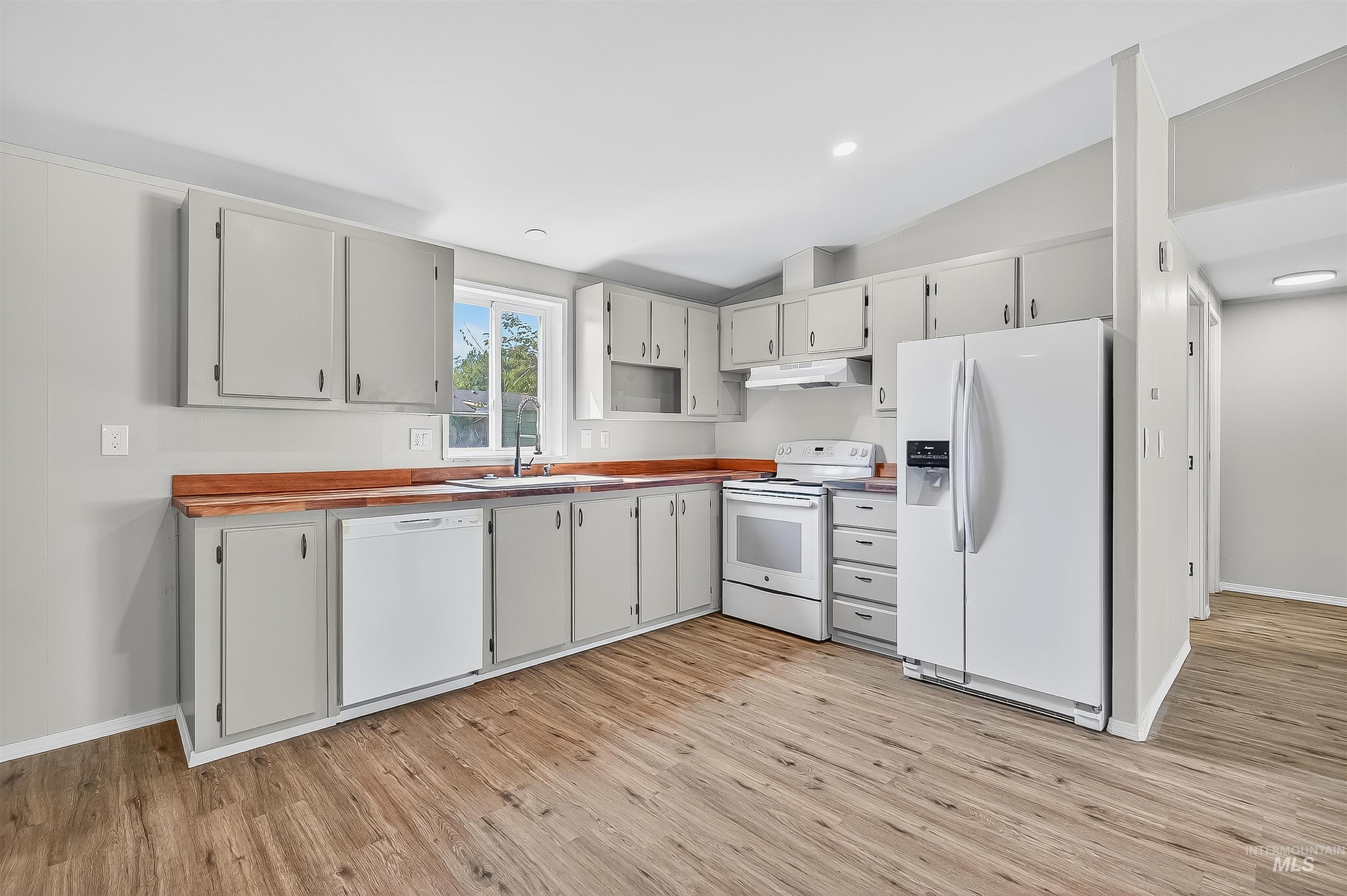 Kitchen with white appliances, lofted ceiling, light wood-style floors, under cabinet range hood, and recessed lighting