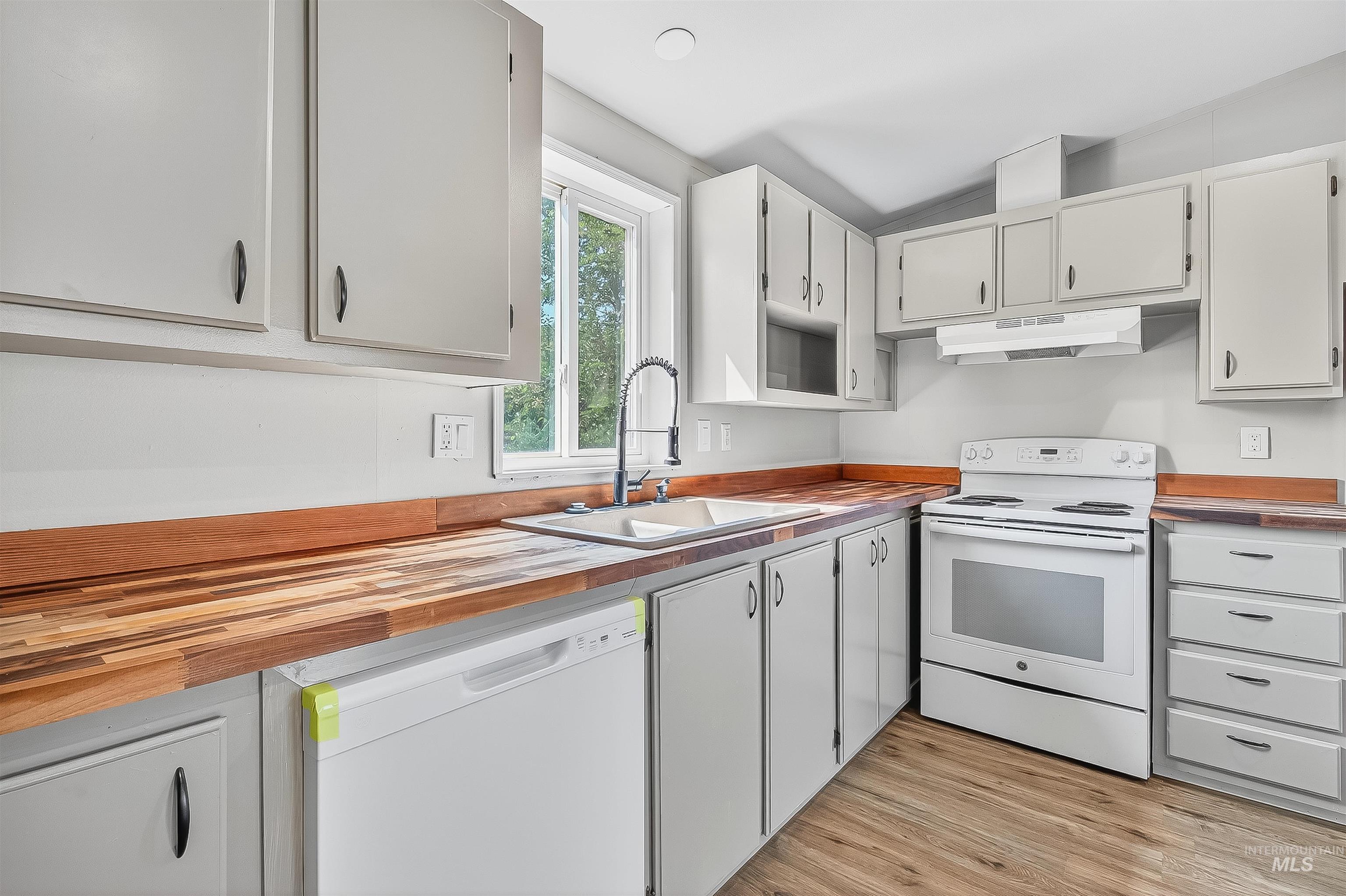 Kitchen with white appliances, wood counters, light wood-type flooring, white cabinetry, and under cabinet range hood