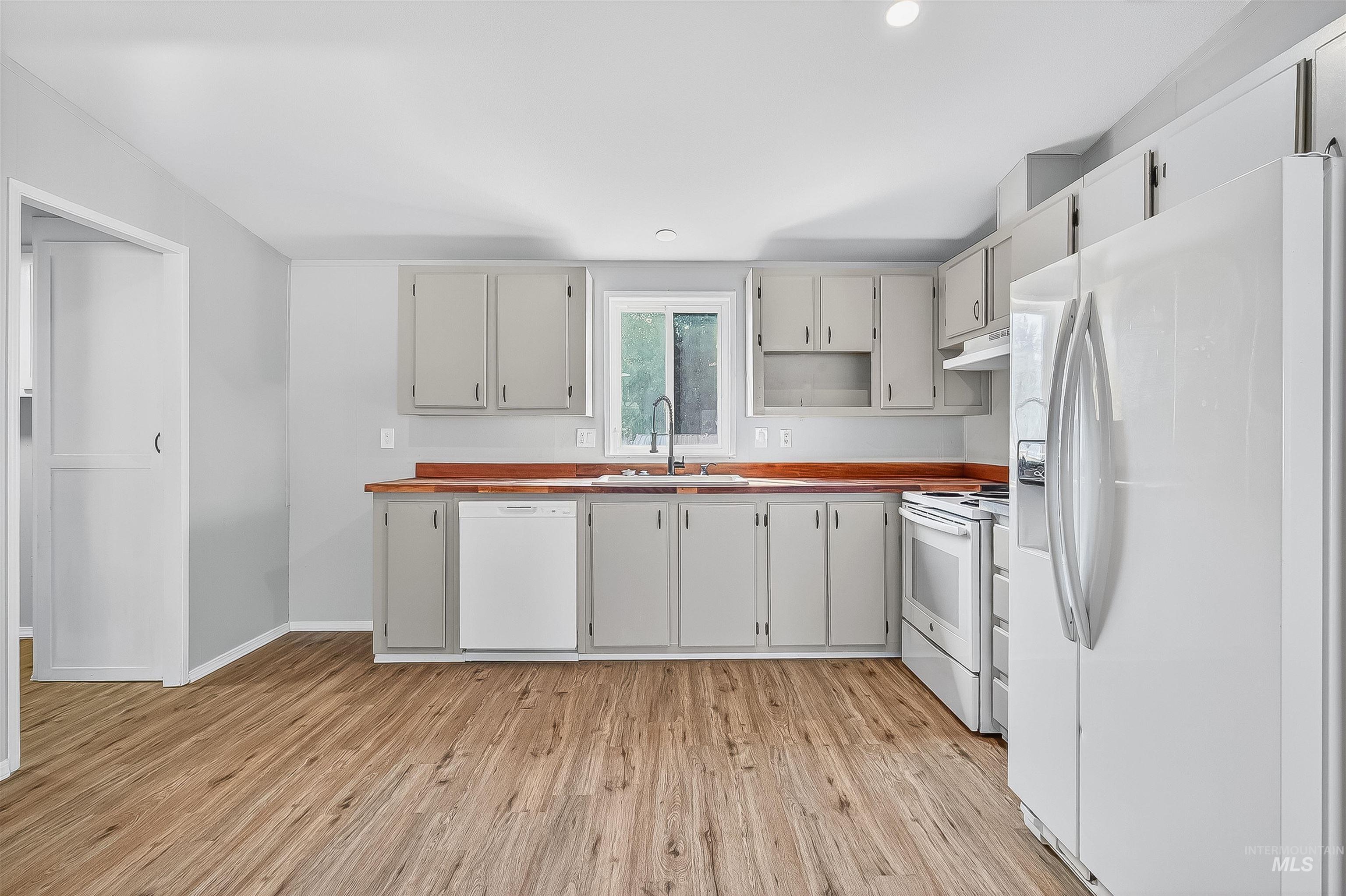 Kitchen with white appliances, light wood-style floors, under cabinet range hood, and recessed lighting