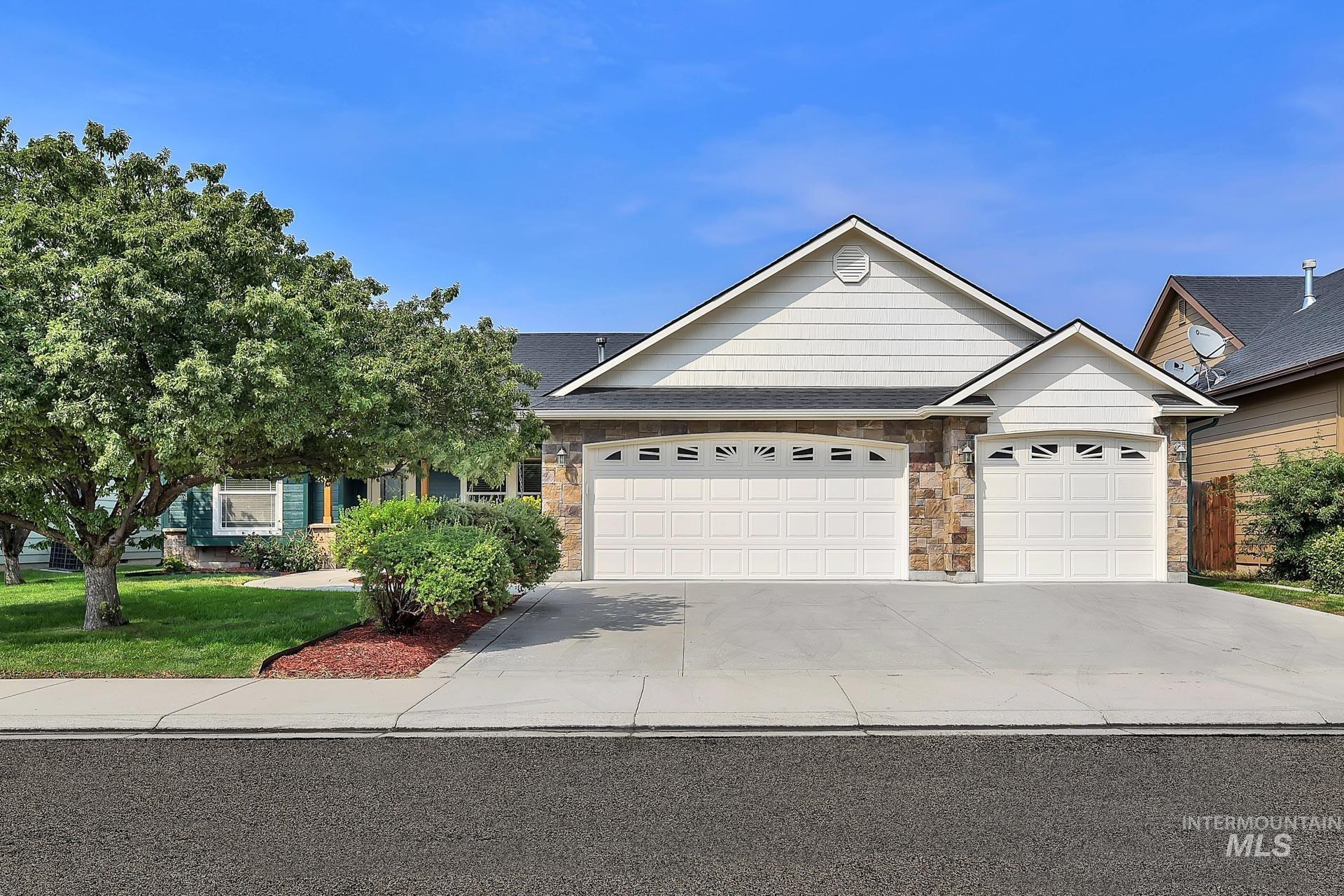 Ranch-style house with nice stone accents, new exterior paint and featuring a front yard with established trees, a porch, concrete driveway, and an attached oversized 3 car garage.