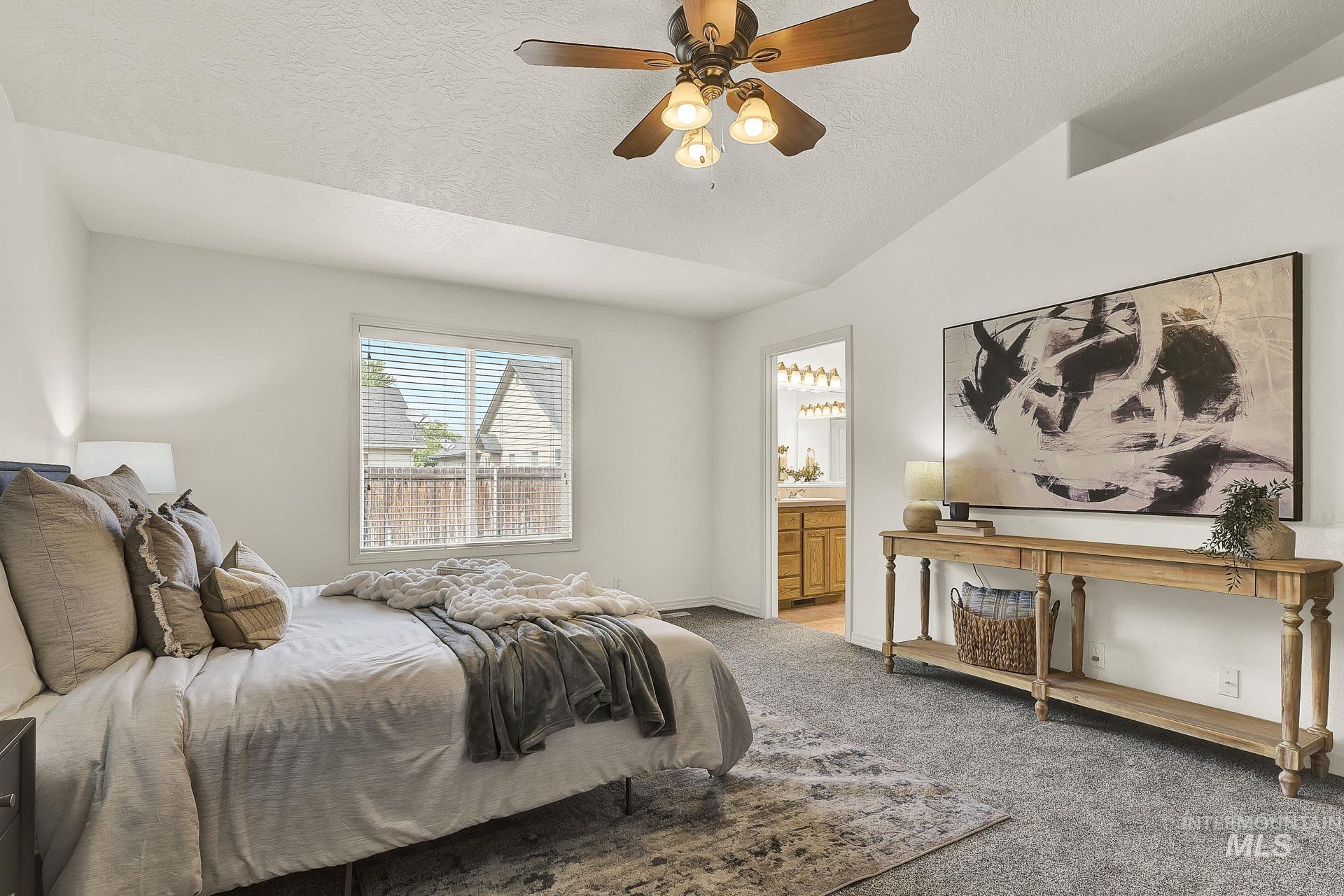 Newly carpeted roomy master bedroom featuring vaulted ceiling, with plenty of natural light, an ensuite bathroom, and ceiling fan. Split floor plan for the bedrooms.