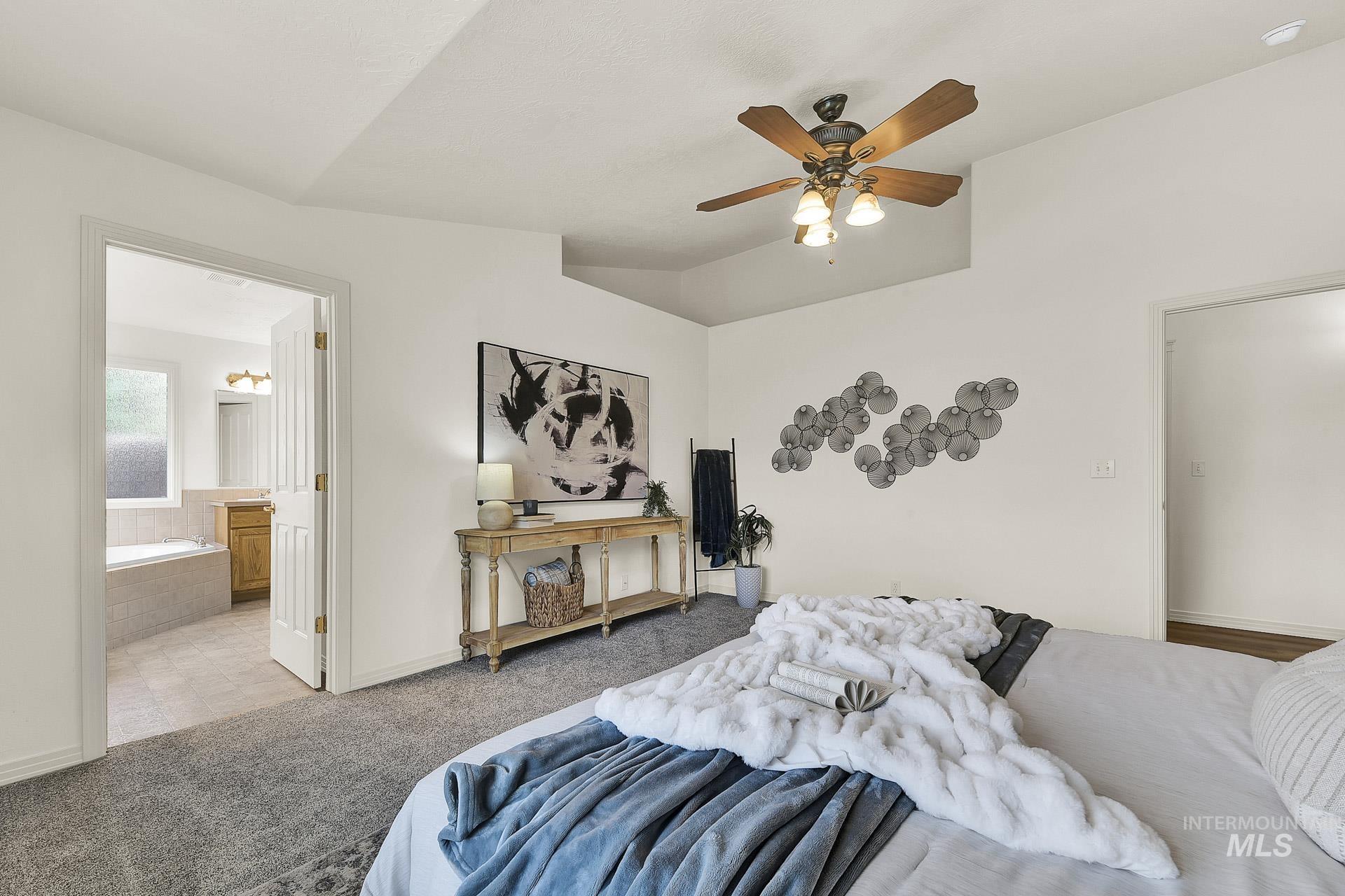 Newly carpeted roomy master bedroom featuring vaulted ceiling, with plenty of natural light, an ensuite bathroom, and ceiling fan. Split floor plan for the bedrooms.