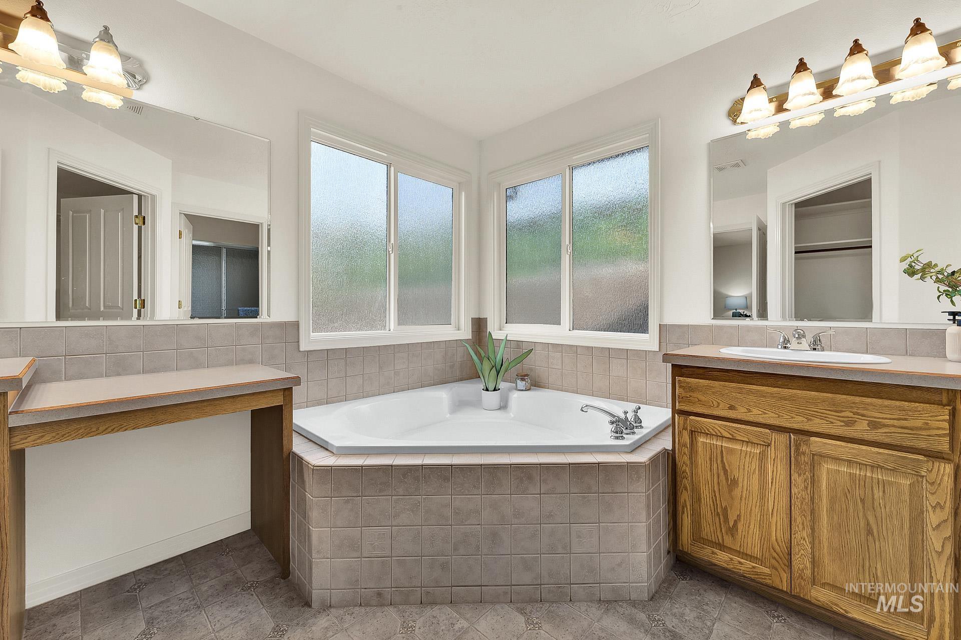 Bathroom with a relaxing corner soaking tub, and separate vanities. Extra large windows with obscure glass to allow natural light in and still have privacy.