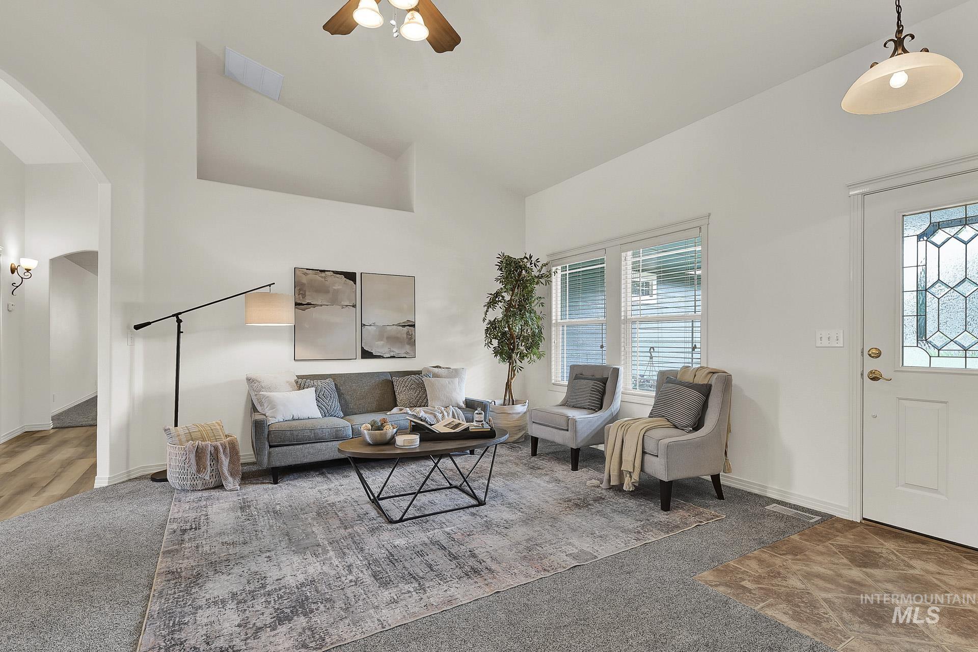Newly Carpeted open concept living area featuring arched doorways, ceiling fan, and high vaulted ceiling with plenty of natural light