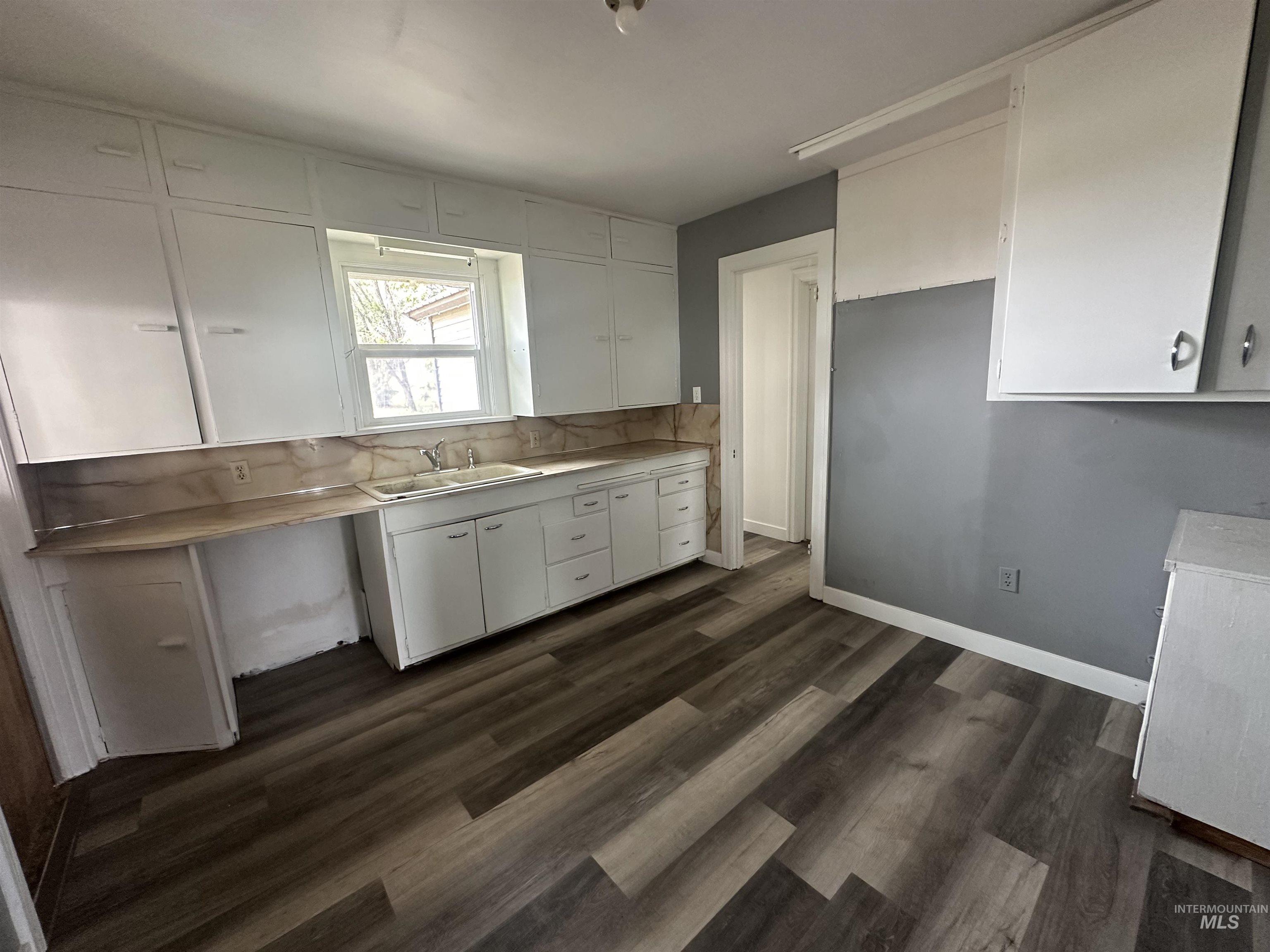 Kitchen with white cabinetry, light countertops, dark wood-type flooring, and backsplash