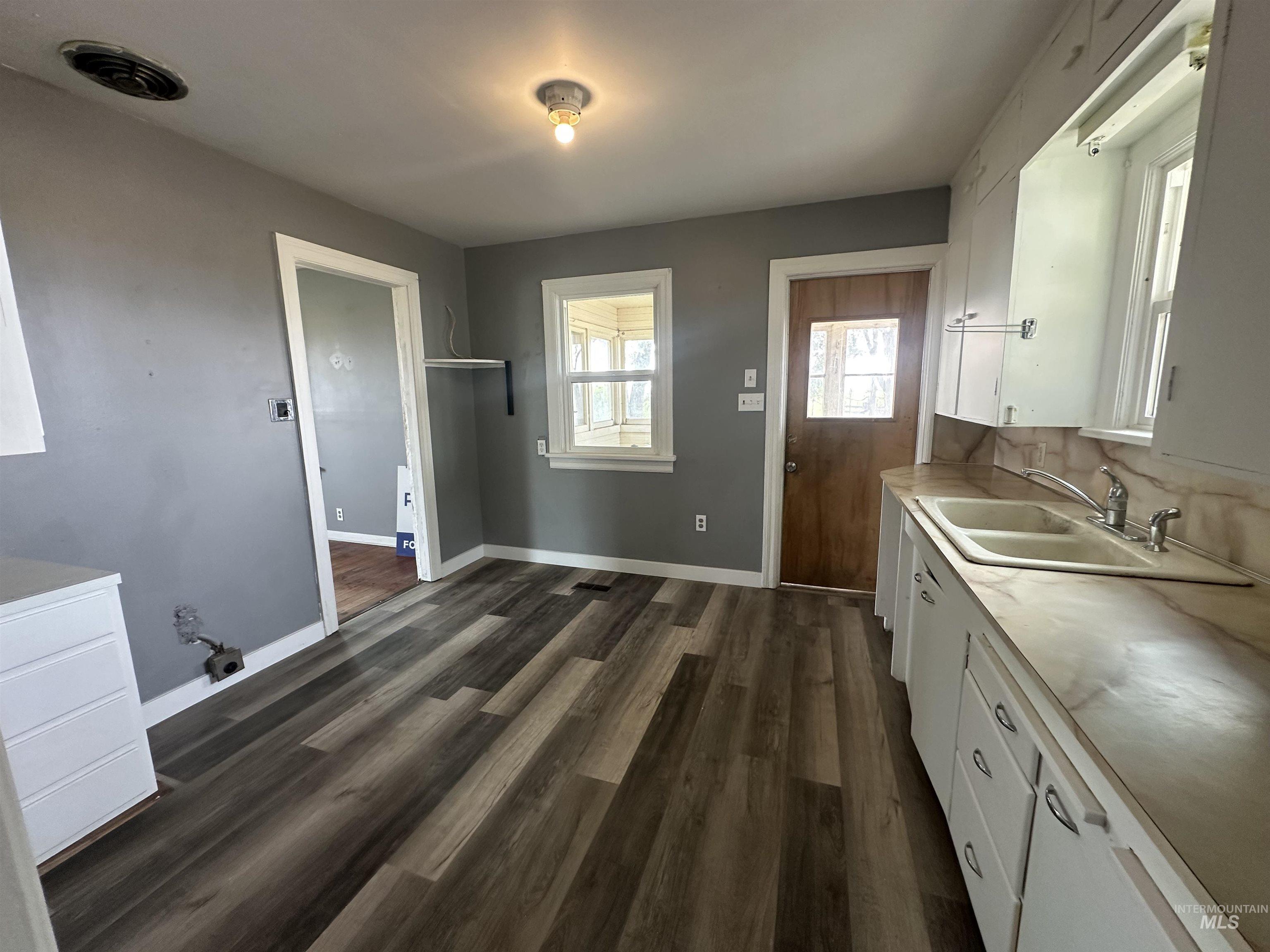 Kitchen featuring white cabinetry, light countertops, dark wood-type flooring, and decorative backsplash