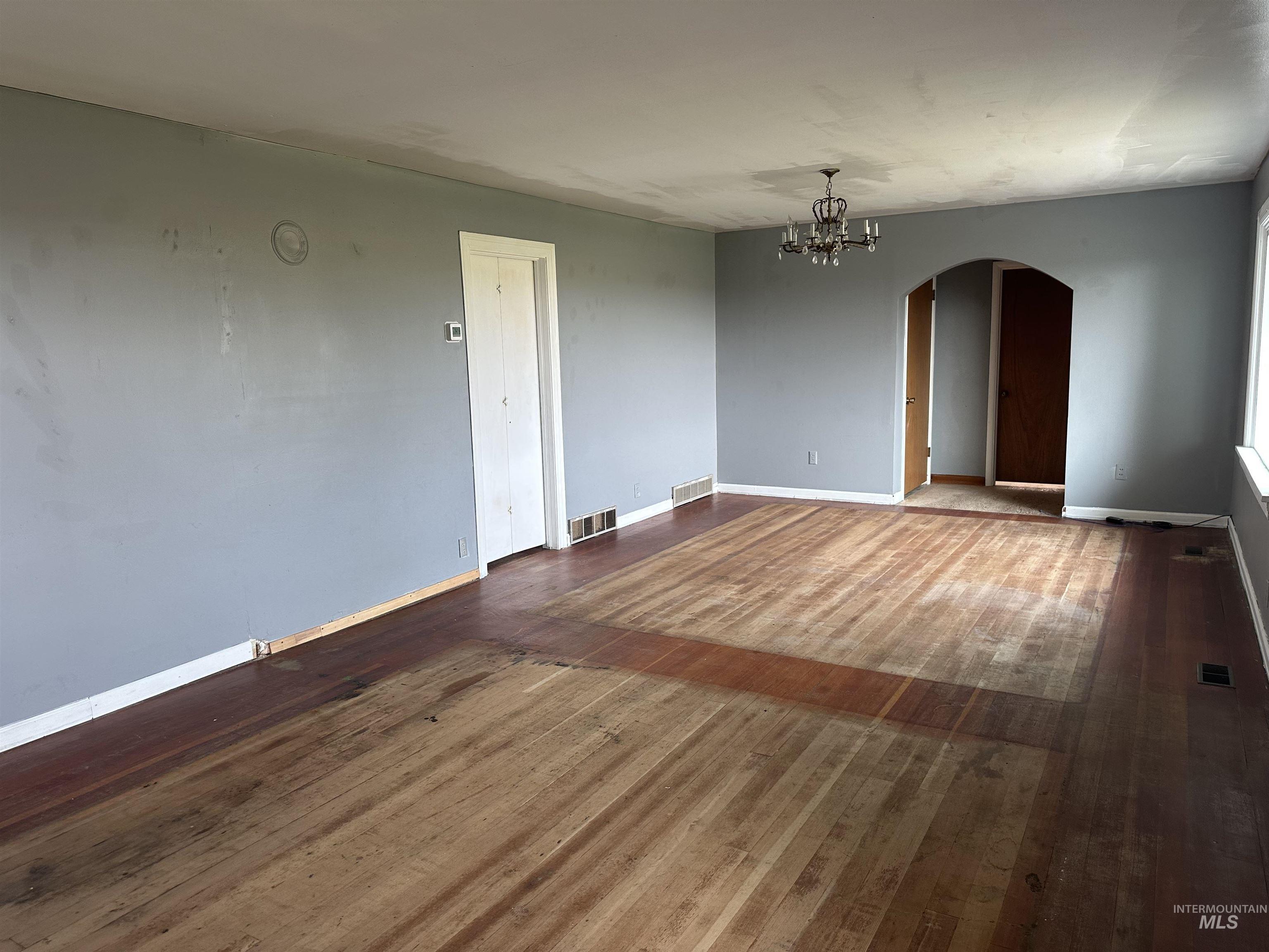 Spare room with dark wood finished floors, arched walkways, and a chandelier