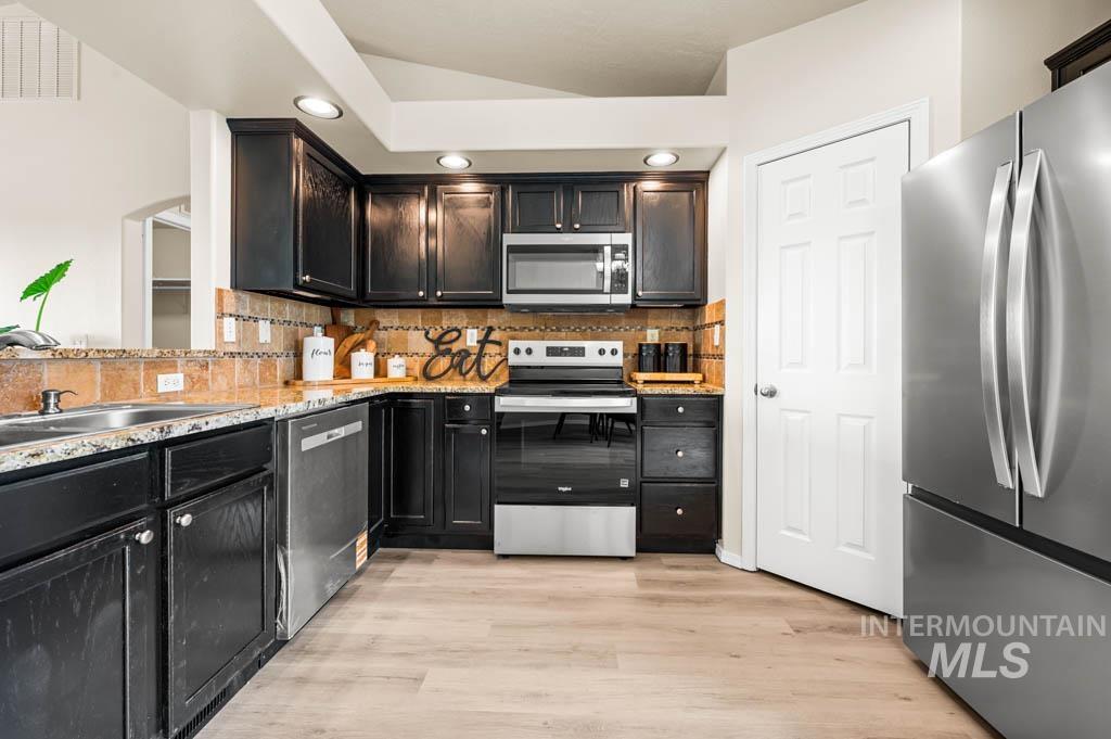 Kitchen featuring appliances with stainless steel finishes, backsplash, light wood-style flooring, recessed lighting, and light stone countertops