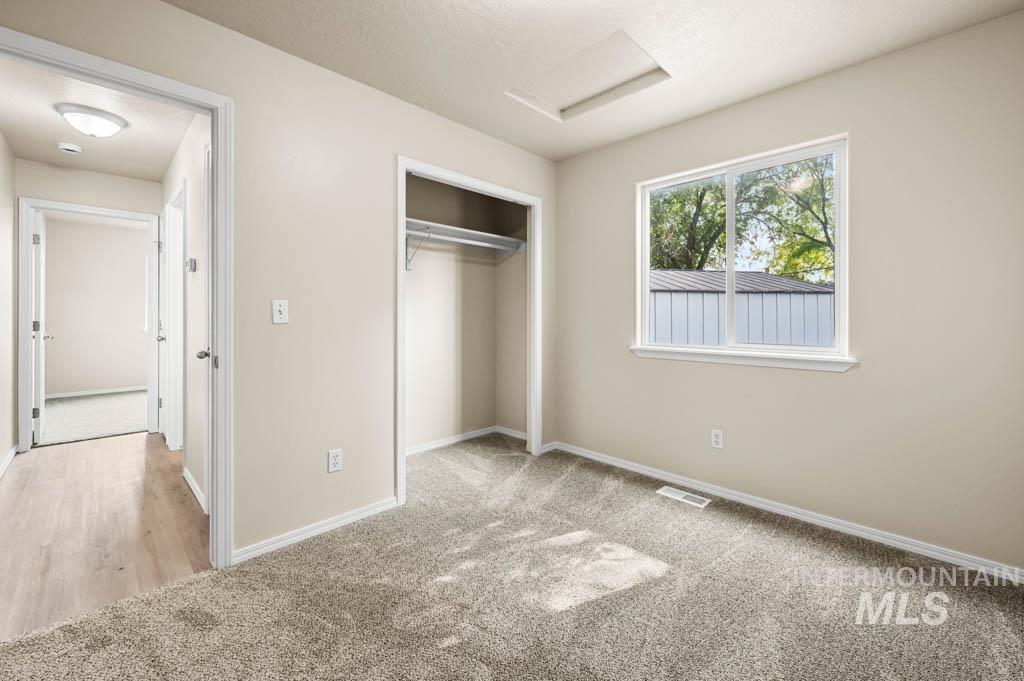 Unfurnished bedroom with attic access, light carpet, and a closet