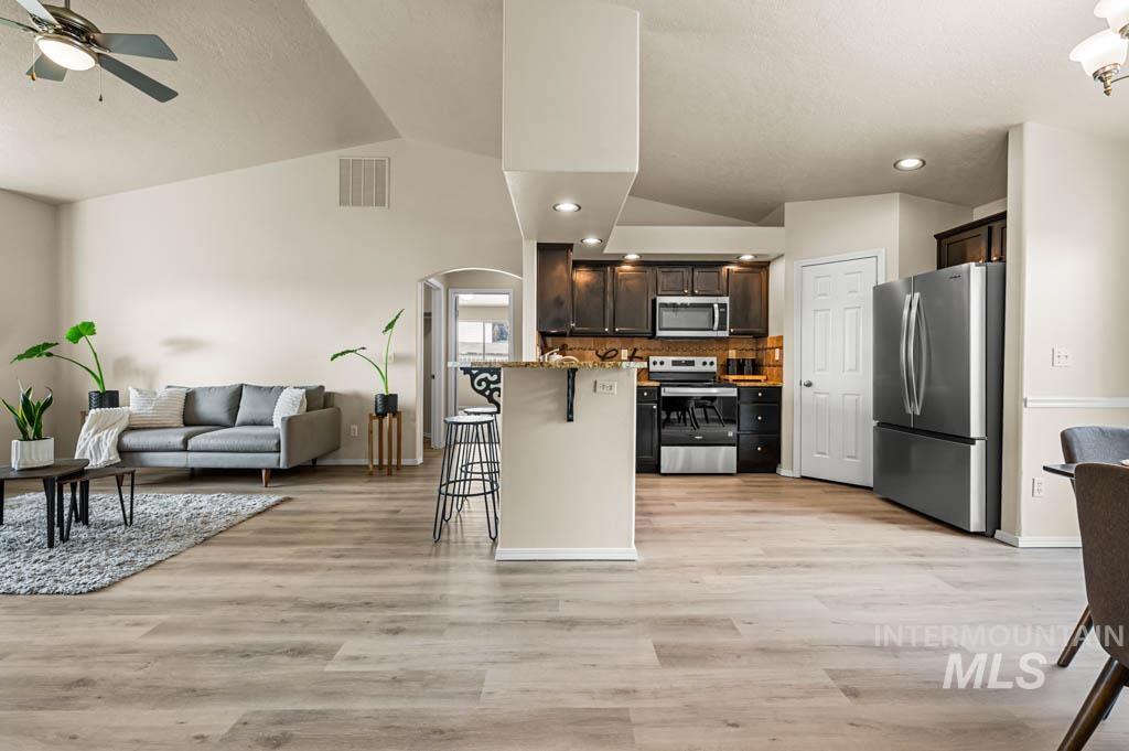 Kitchen with a breakfast bar area, stainless steel appliances, open floor plan, dark brown cabinets, and decorative backsplash