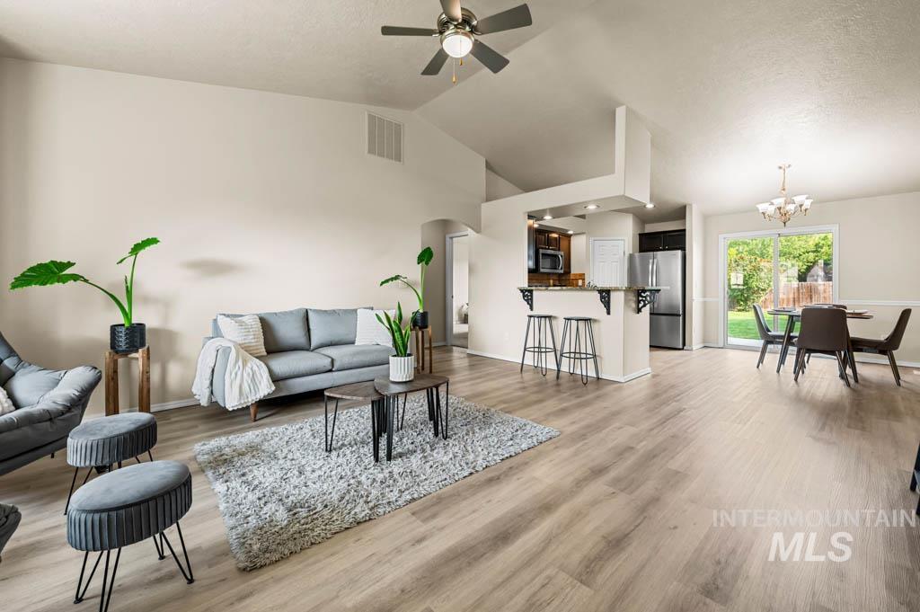 Living area with light wood finished floors, arched walkways, a ceiling fan, a textured ceiling, and a chandelier
