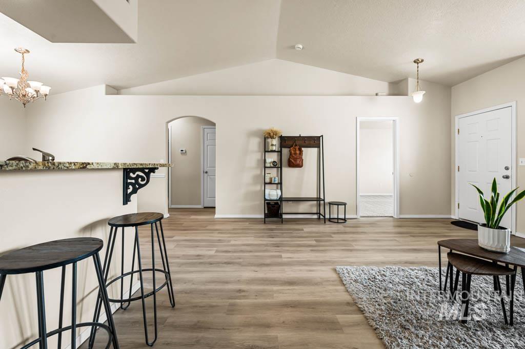 Living room featuring light wood-style floors, arched walkways, vaulted ceiling, and a chandelier